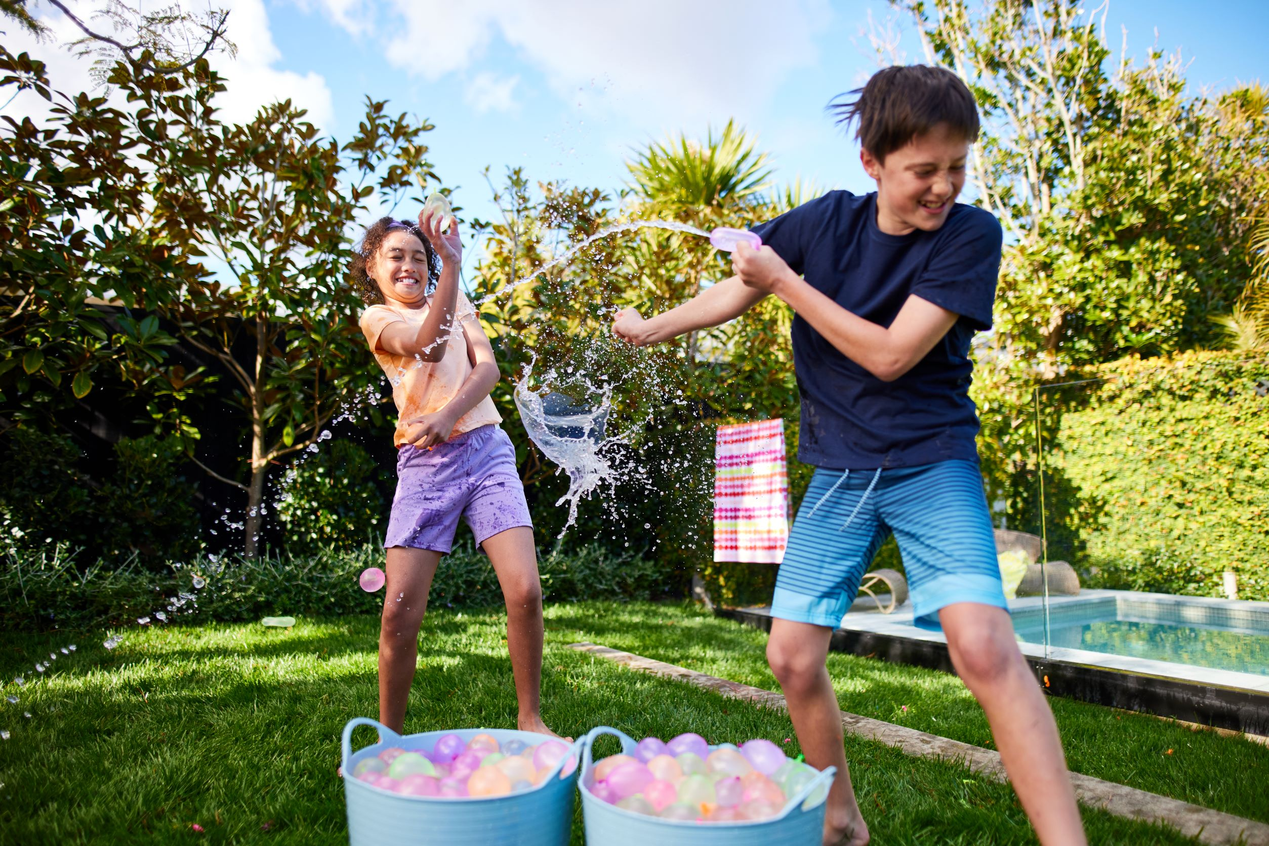 Zwei Kinder spielen mit Wasserbomben, spritzen Wasser im sonnigen Freien.