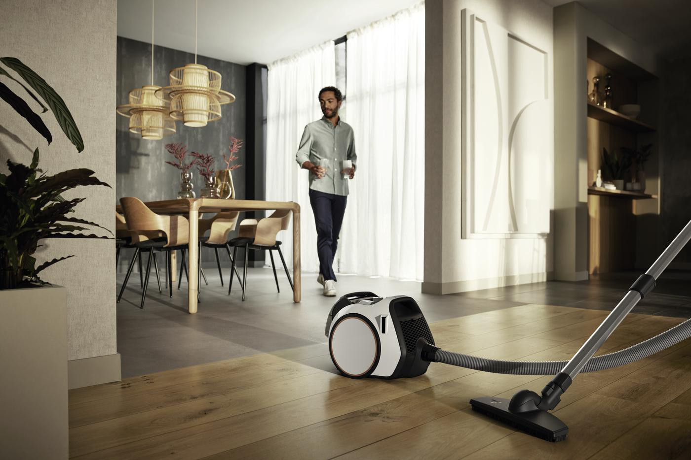 Mann geht in der Nähe eines Staubsaugers. Holzboden und modernes Interieur. Tisch mit Hängelampen.