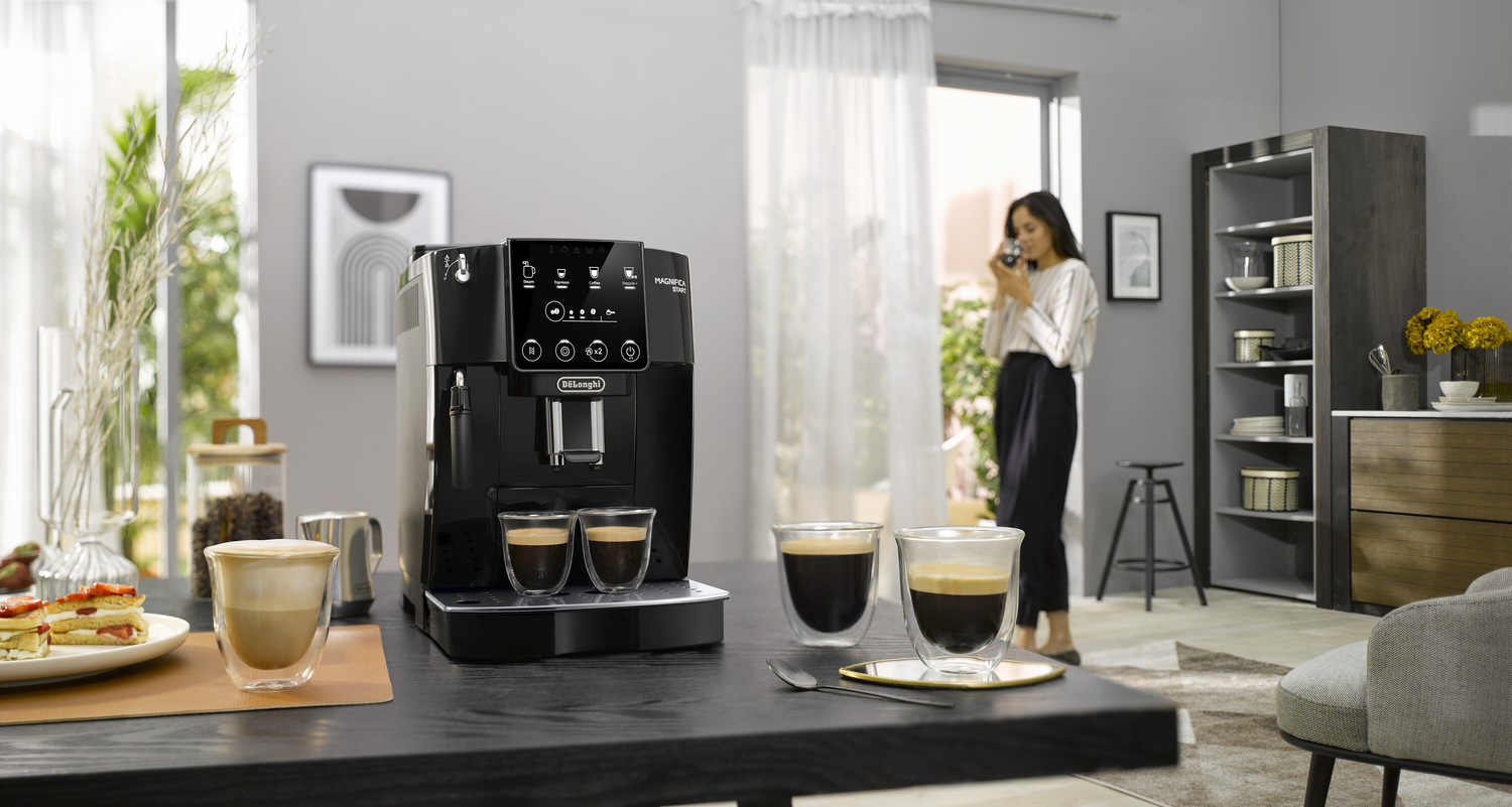 Máquina de espresso negra. Dos vasos de café en mesa. Mujer bebiendo.