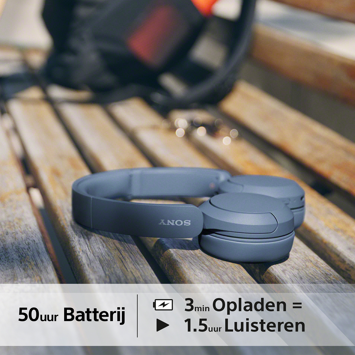 Blauwe koptelefoon op een houten bank. Tekst: 50 uur Batterij. 3min Opladen = 1.5uur Luisteren.