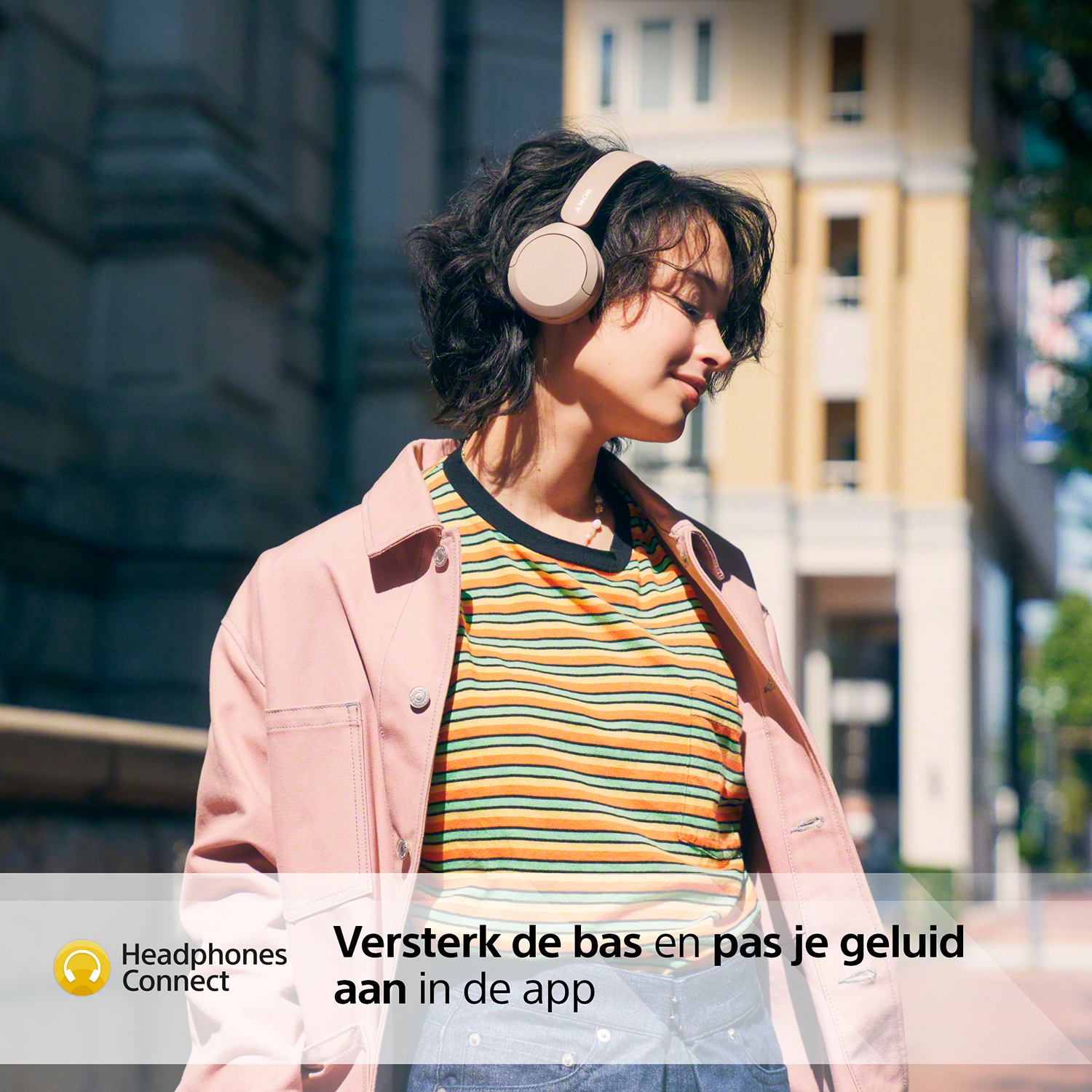 Vrouw die naar een koptelefoon luistert in een stedelijke omgeving. Gebouwen op de achtergrond. Tekst onderaan.