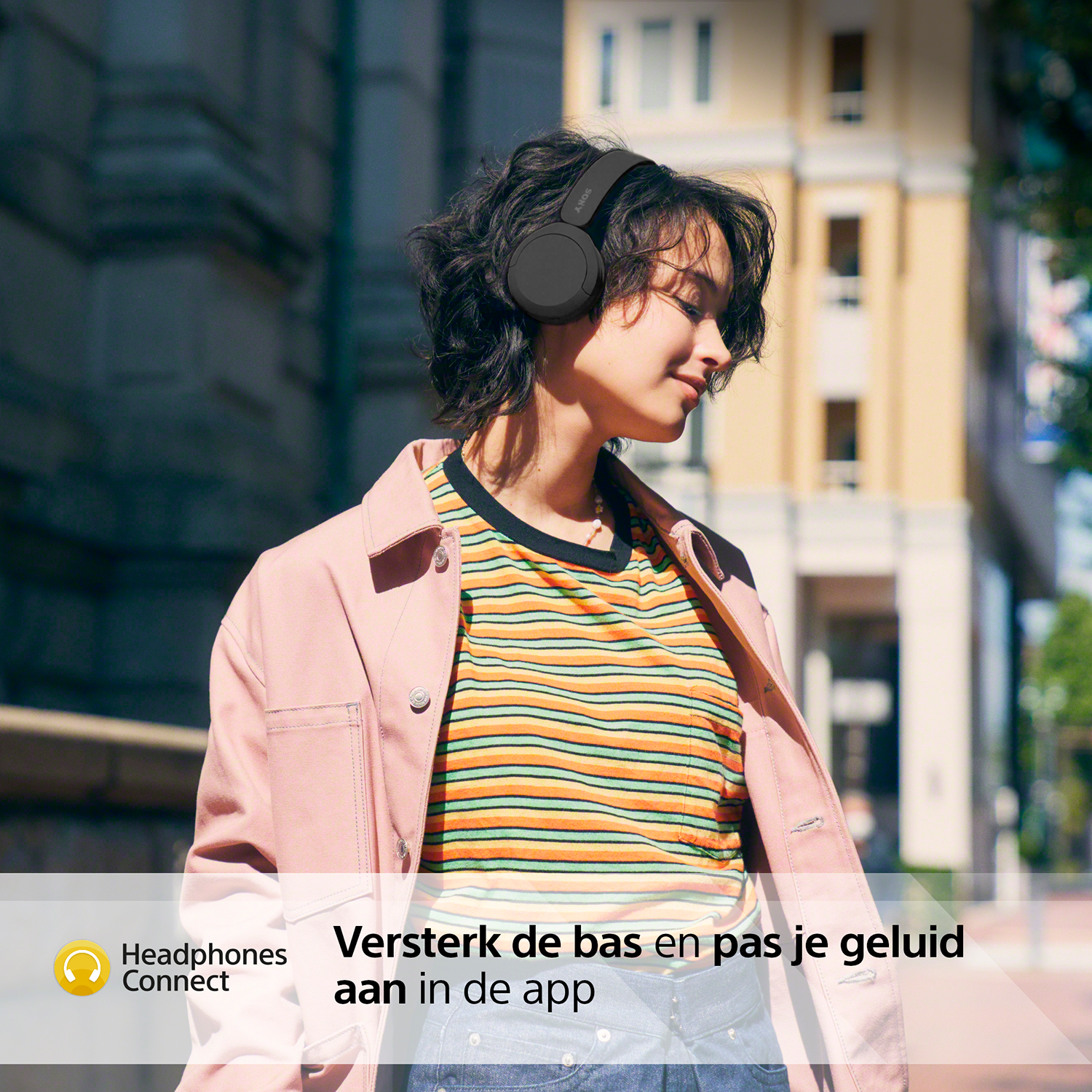 Vrouw met een koptelefoon, glimlachend op een stadsstraat.