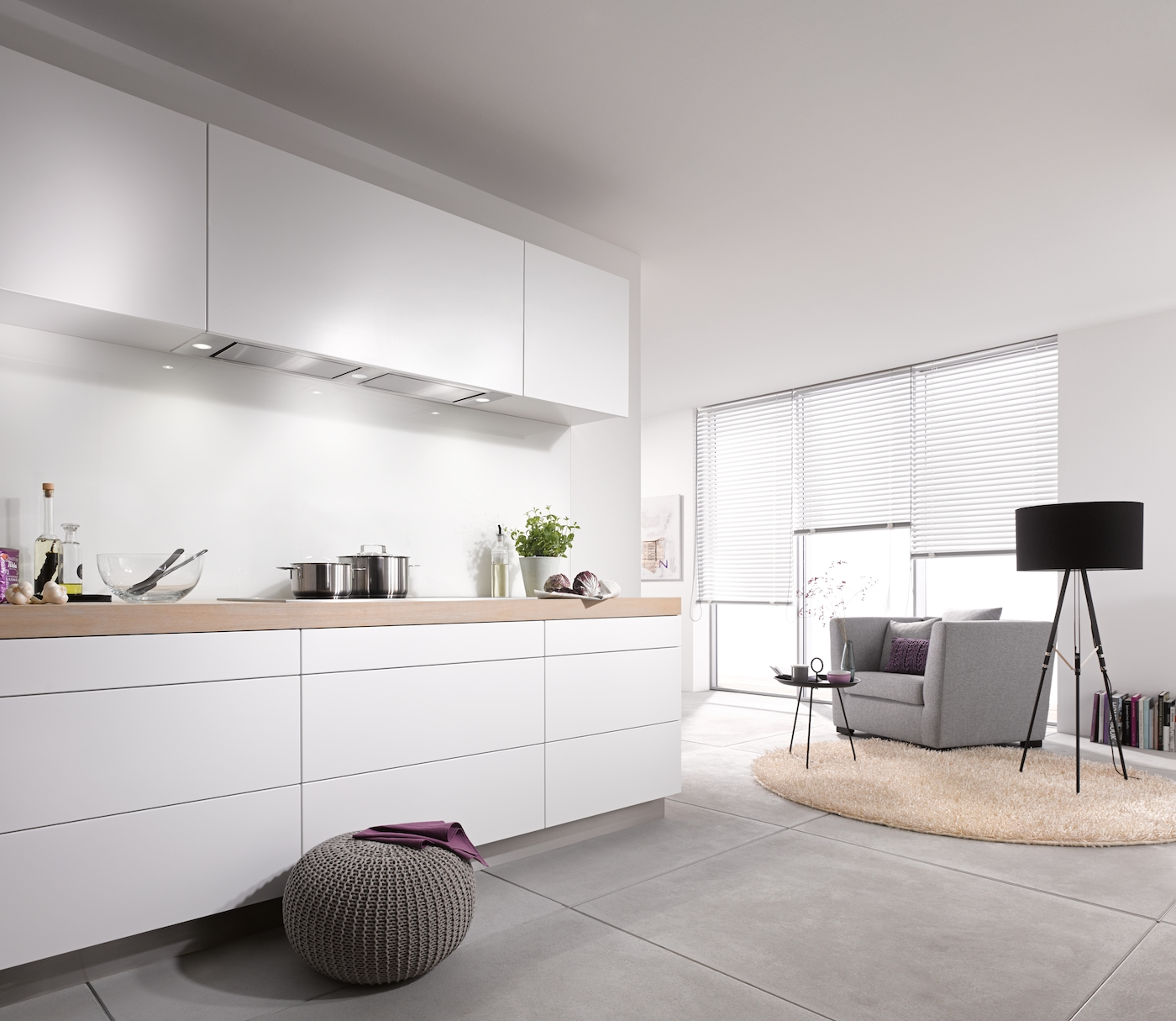 Moderne weiße Küche mit Holzarbeitsplatte, grauem Sessel und schwarzer Stehlampe.