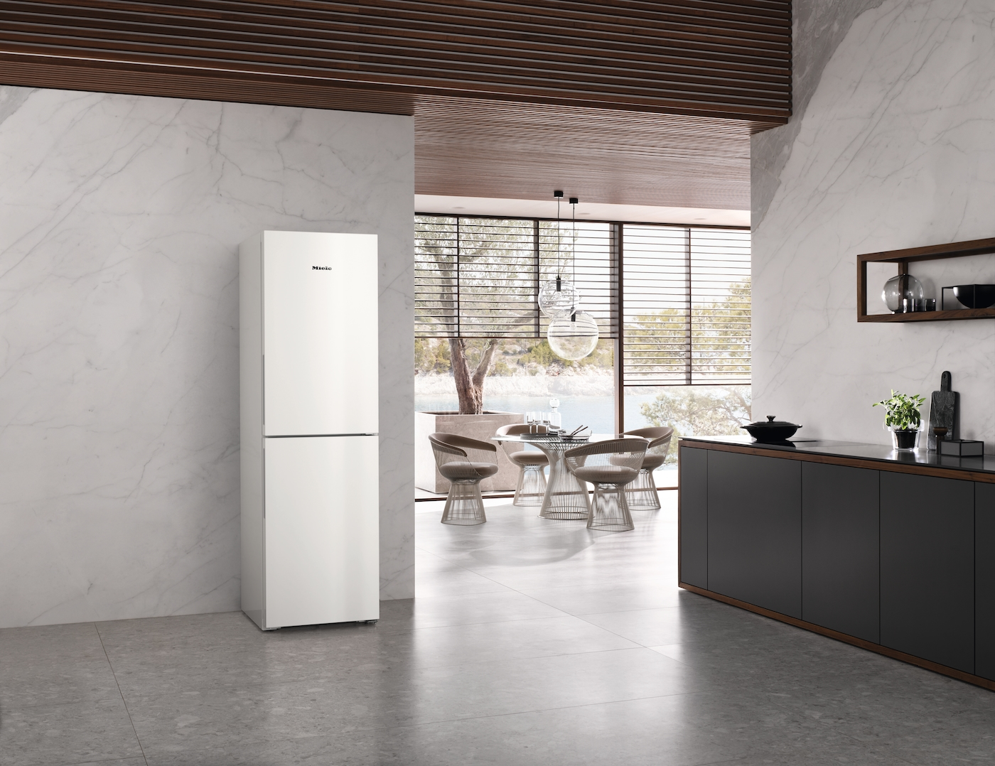Ein moderner weißer Kühlschrank steht in einer Marmorküche neben einem Essbereich mit Blick nach draußen.