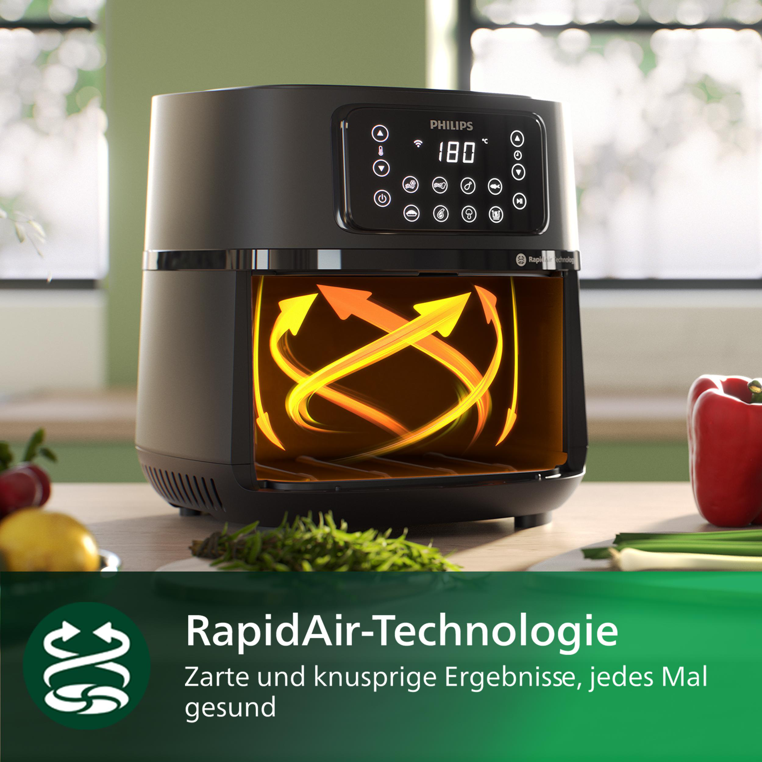 Schwarze Heißluftfritteuse mit Display vorne. Innen orangefarbenes Licht vom Kochen. Rote Paprika rechts.