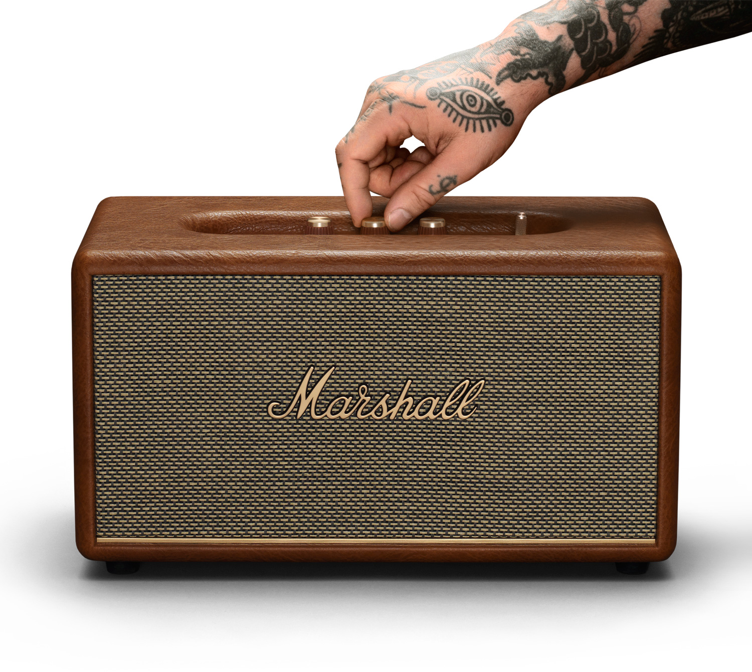 Une main tatouée ajustant le bouton de volume sur une enceinte Marshall marron.