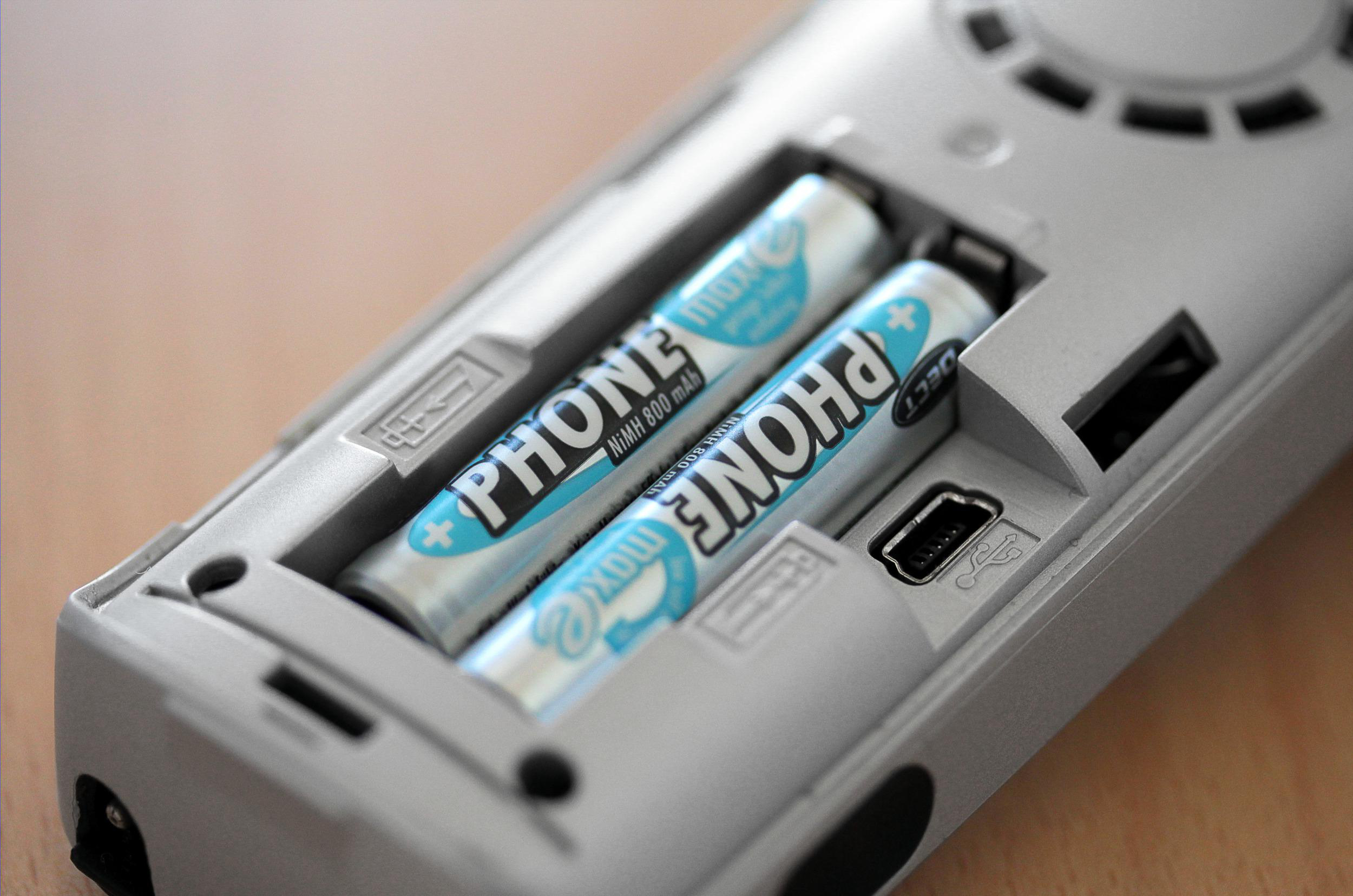 Nahaufnahme des Batteriefachs eines Telefons. Zwei AA-Batterien sind sichtbar, beschriftet mit 'PHONE'.