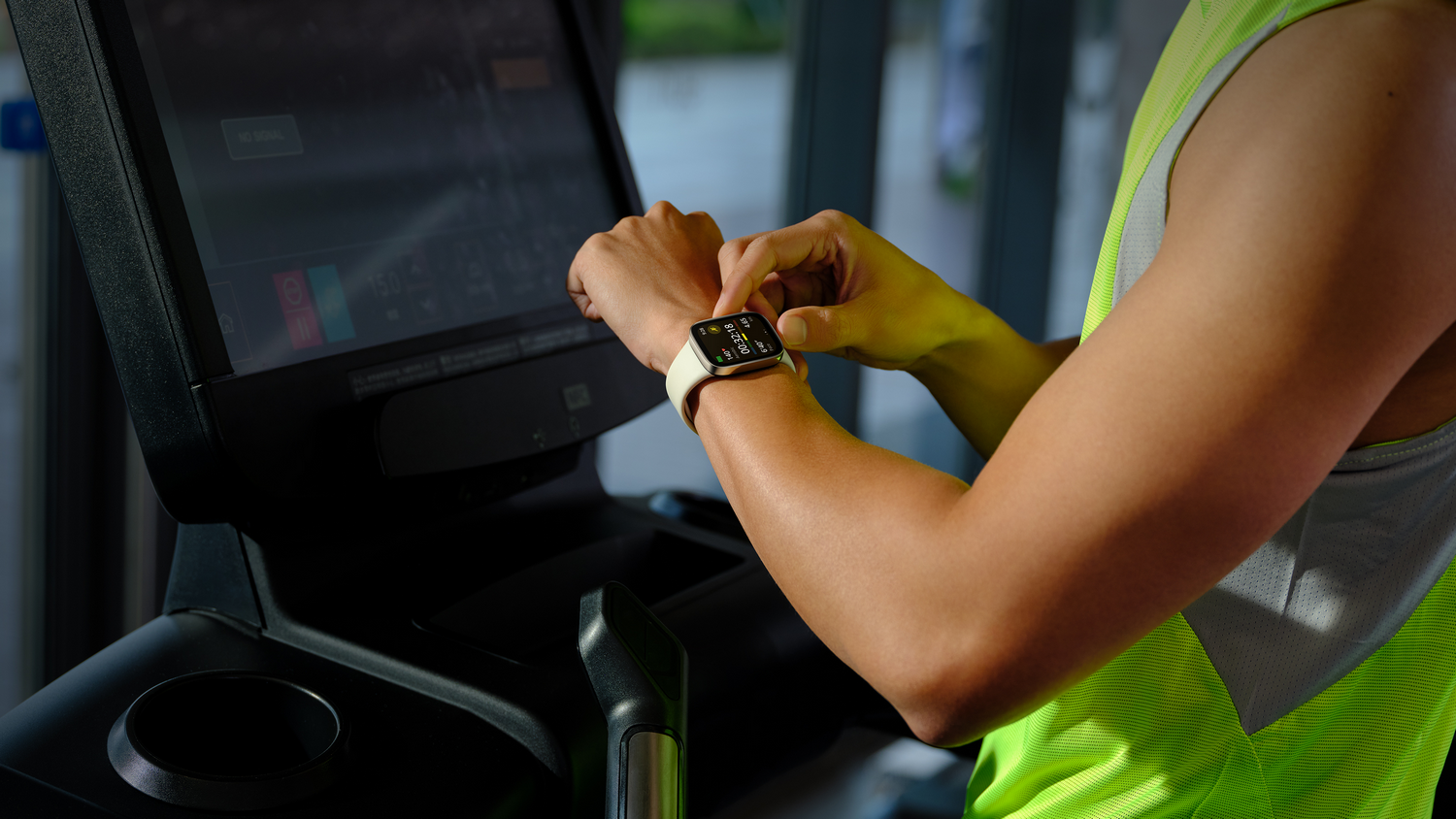 Una persona en una cinta de correr, mirando su reloj inteligente. Entorno de gimnasio.