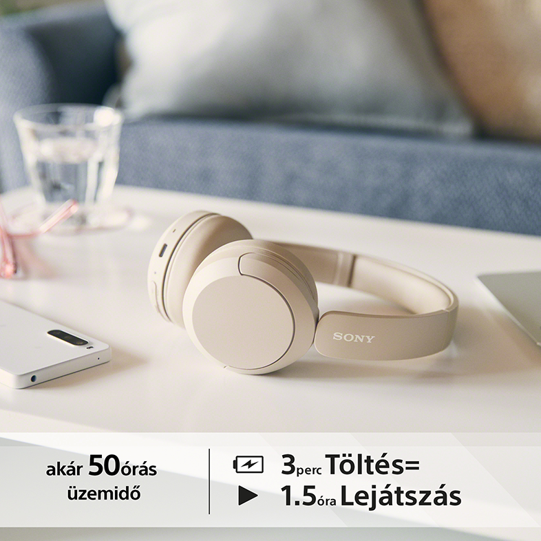Bézs fejhallgató fehér felületen. Telefon és egy pohár víz a háttérben.