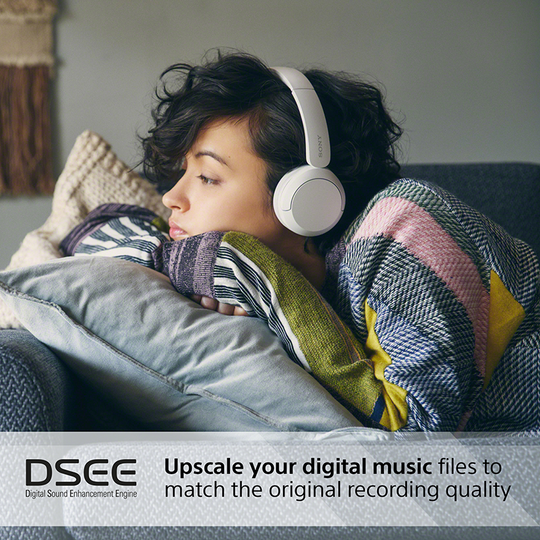 Egy nő fehér fejhallgatót visel, egy párnával pihen. Szöveg: Upscale your digital music.