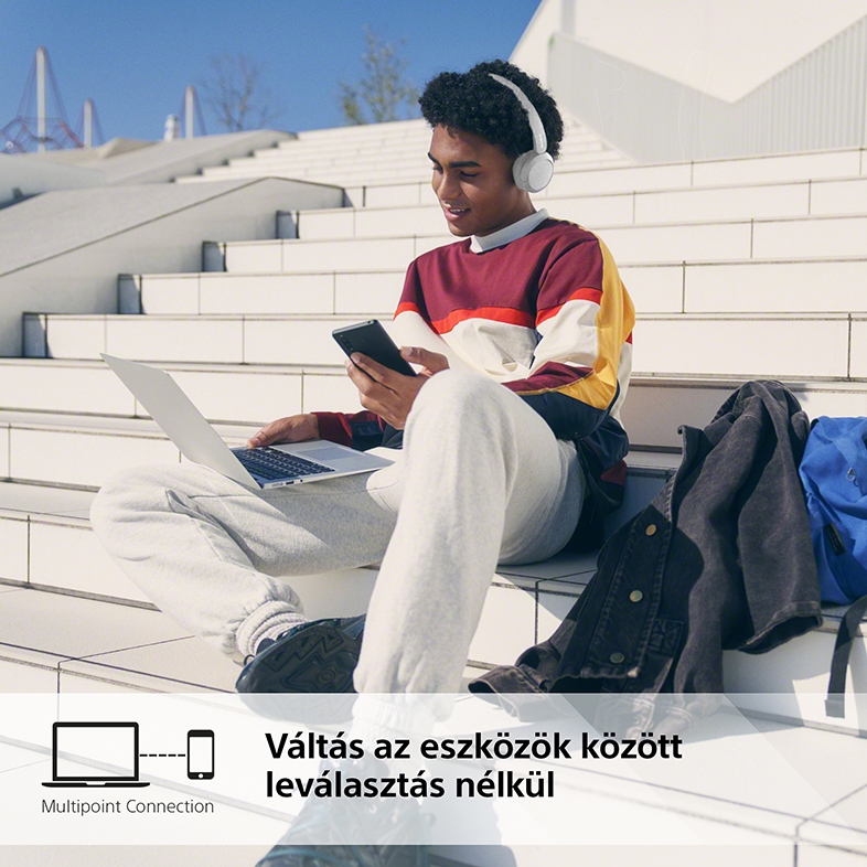 Egy fiatalember lépcsőn ül, laptopot és telefont használ, fejhallgatóval. Szöveg a több eszközös használatról.