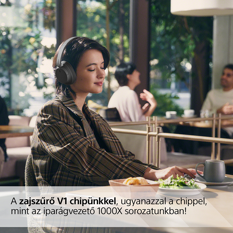 Egy nő egy kávézóban fejhallgatóval, lefelé néz, kávéval és étellel.