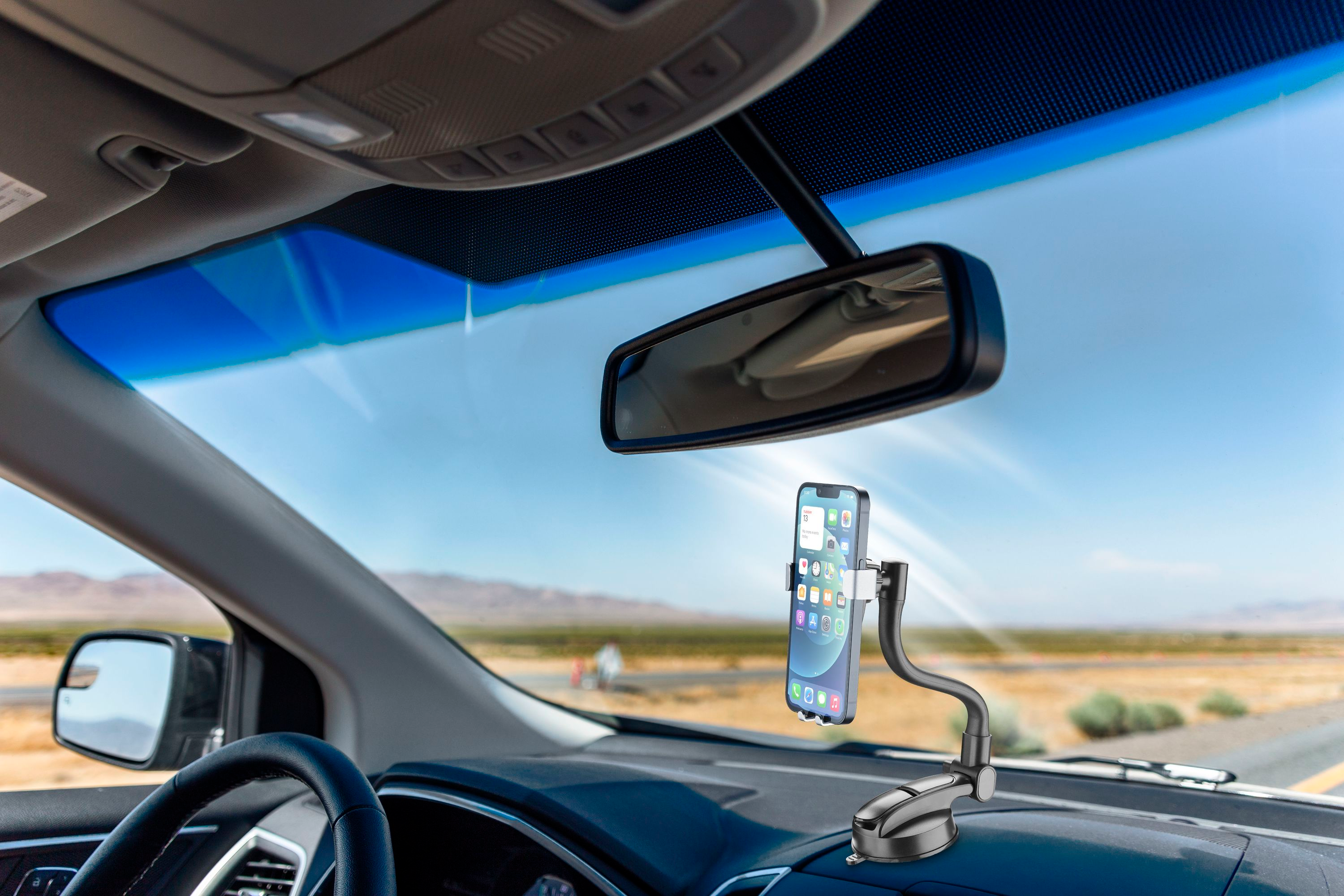 Un telefono montato sul cruscotto di un'auto, parabrezza e strada visibili sullo sfondo, giornata di sole.