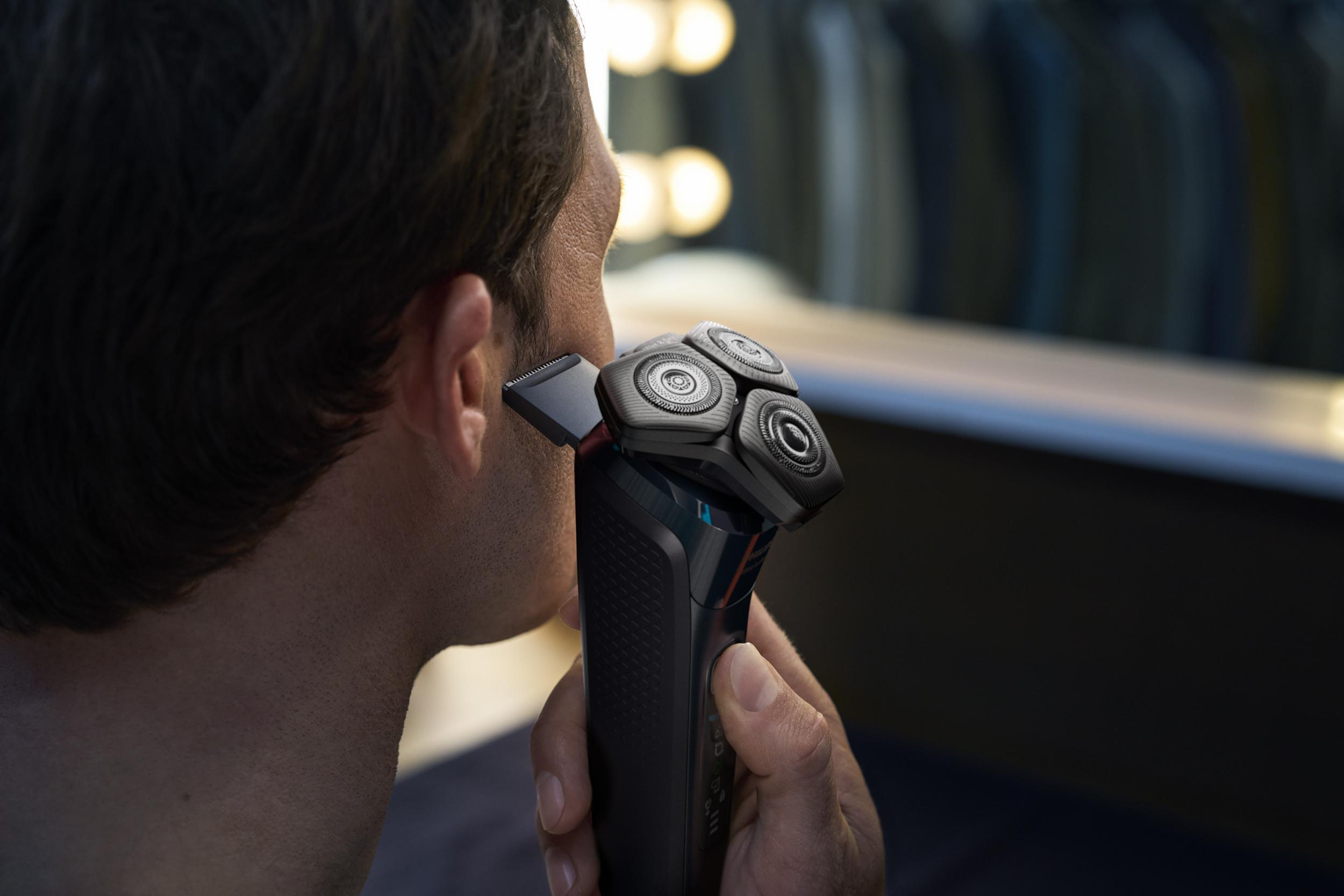 Mann rasiert sich mit einem schwarzen Elektrorasierer. Fokus auf Rasiererkopf und Gesicht.