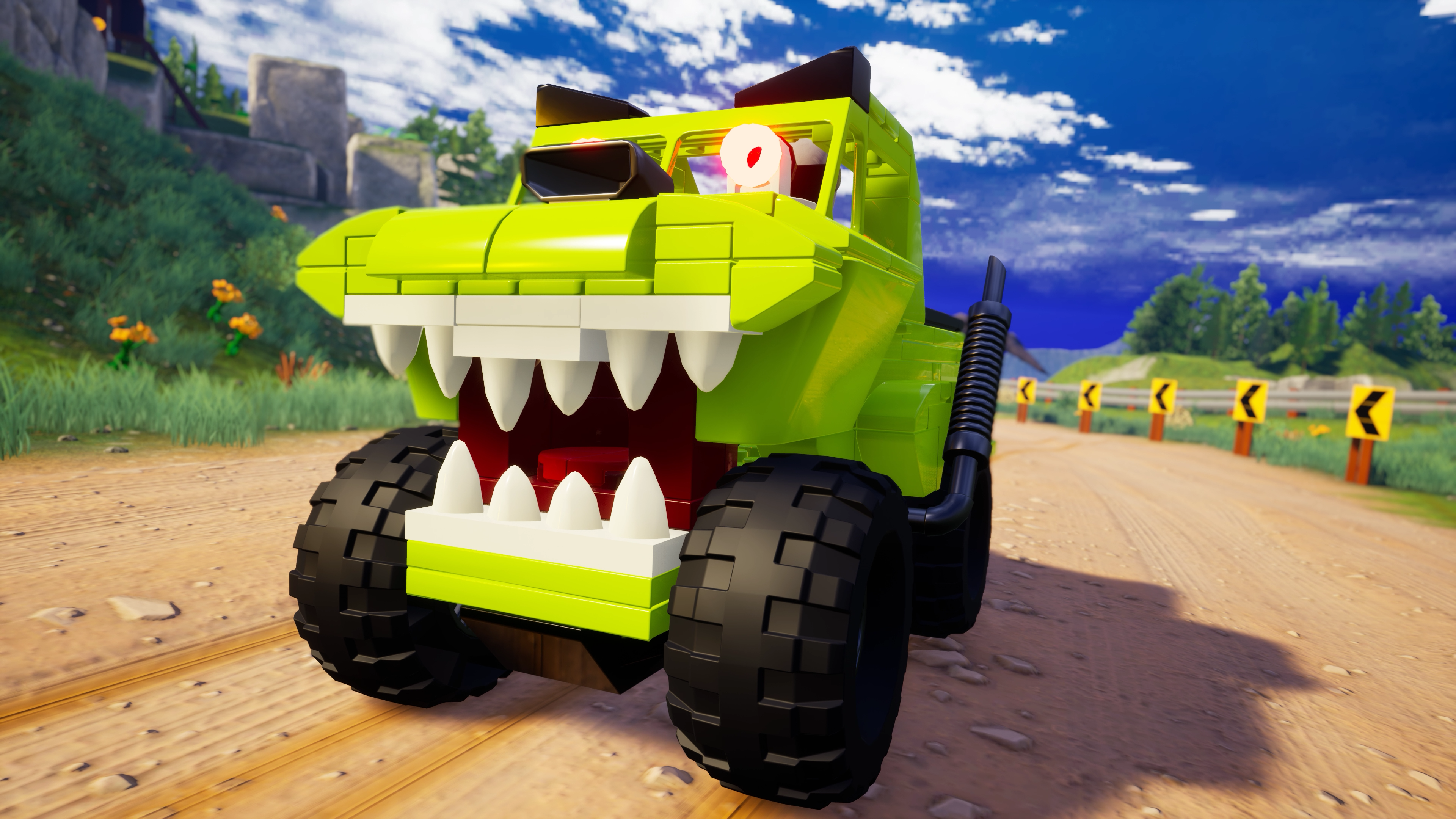 Grünes Spielzeugauto mit Monstertruck-Design, auf einer Schotterstraße mit blauem Himmel im Hintergrund.