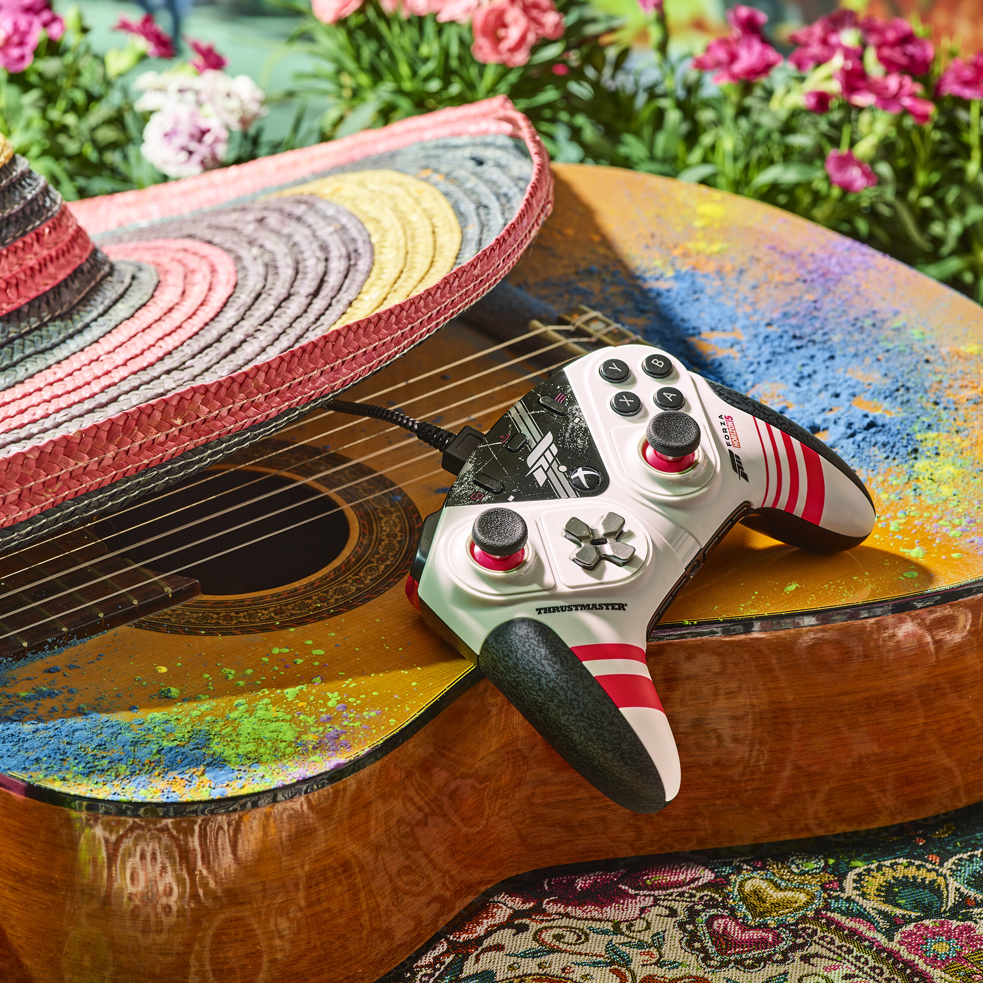 Ein Gamecontroller auf einer bemalten Gitarre mit Sombrero und Blumen im Hintergrund.