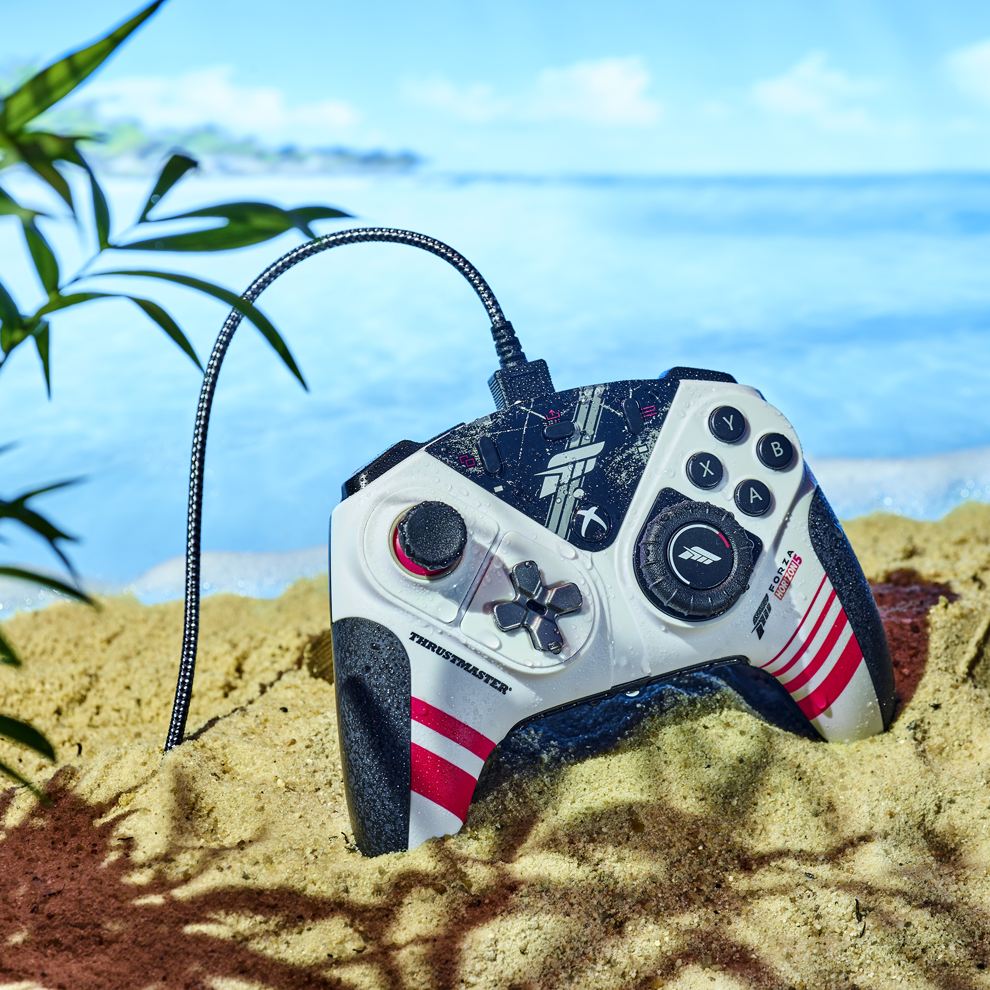 Spiel-Controller auf Sand mit Ozean- und Himmels-Hintergrund. Der Controller hat rot-weiße Streifen.
