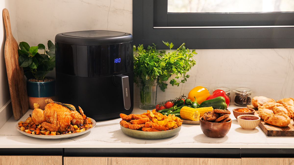 Freidora de aire con pollo cocido, papas fritas y otros alimentos, junto con ingredientes.