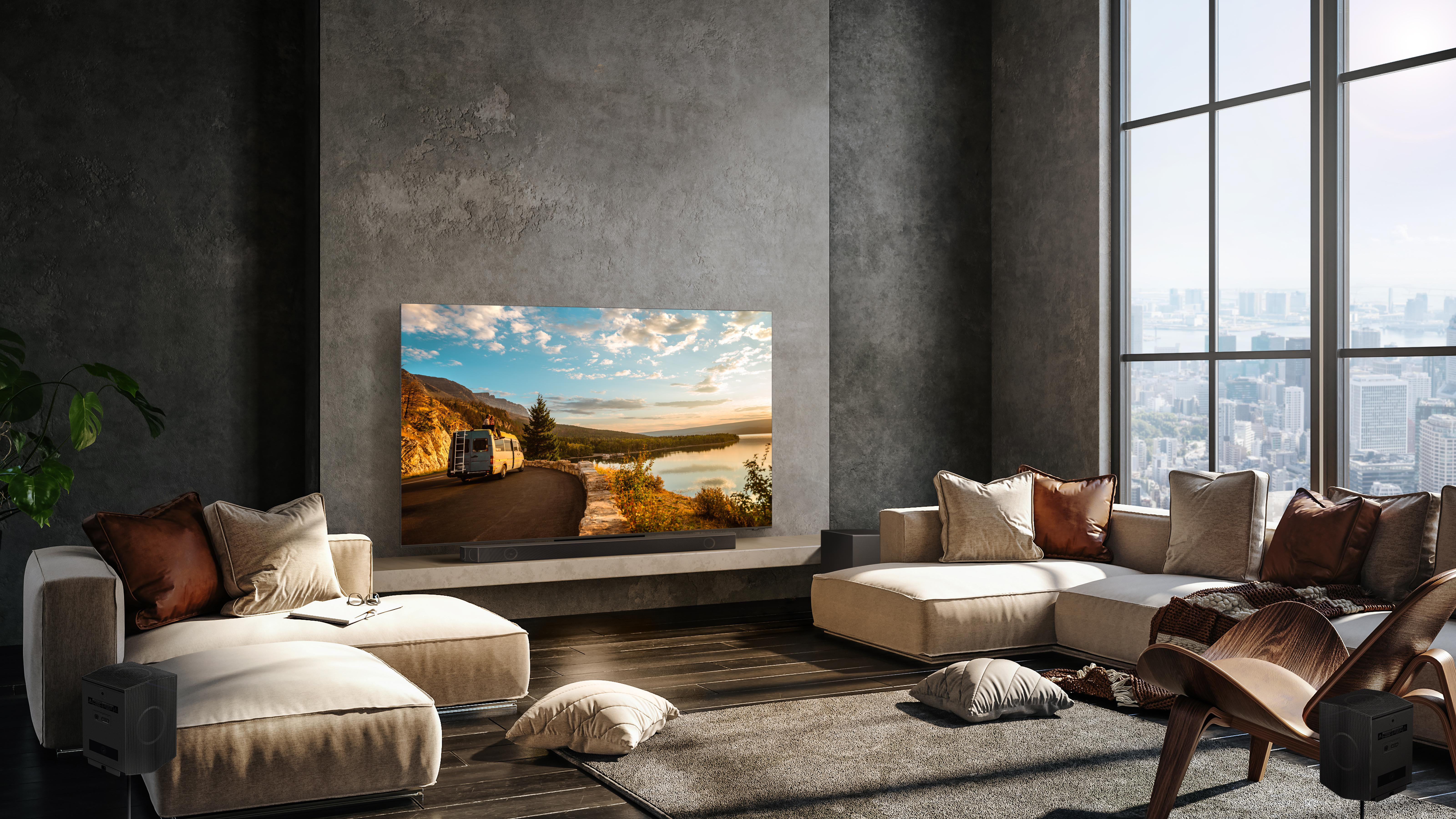 Wohnzimmer mit großem Fernseher, Couch, Stühlen und Lautsprechern. Stadtblick draußen.