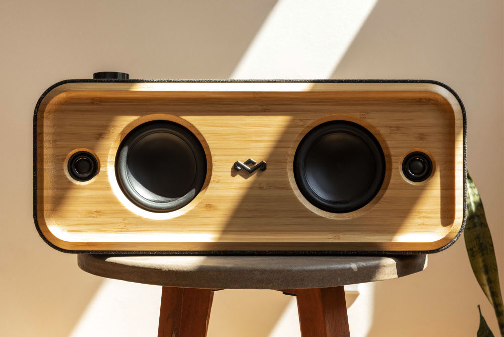 Wooden speaker with two black speakers and a logo. It sits on a small wooden stool.