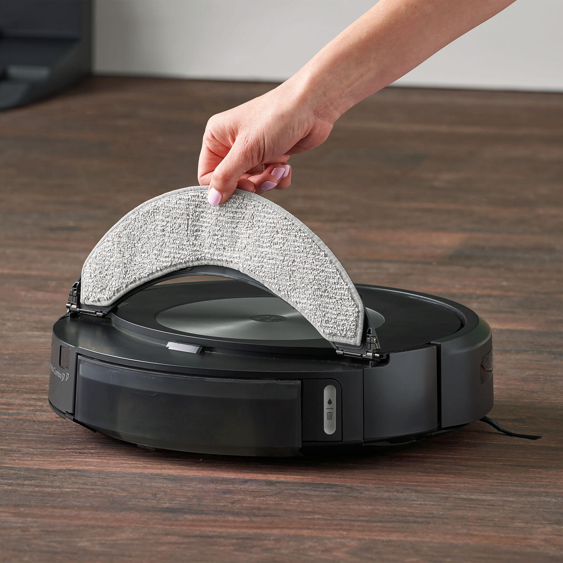 Eine Hand legt ein graues Reinigungspad auf einen schwarzen Roboterstaubsauger.