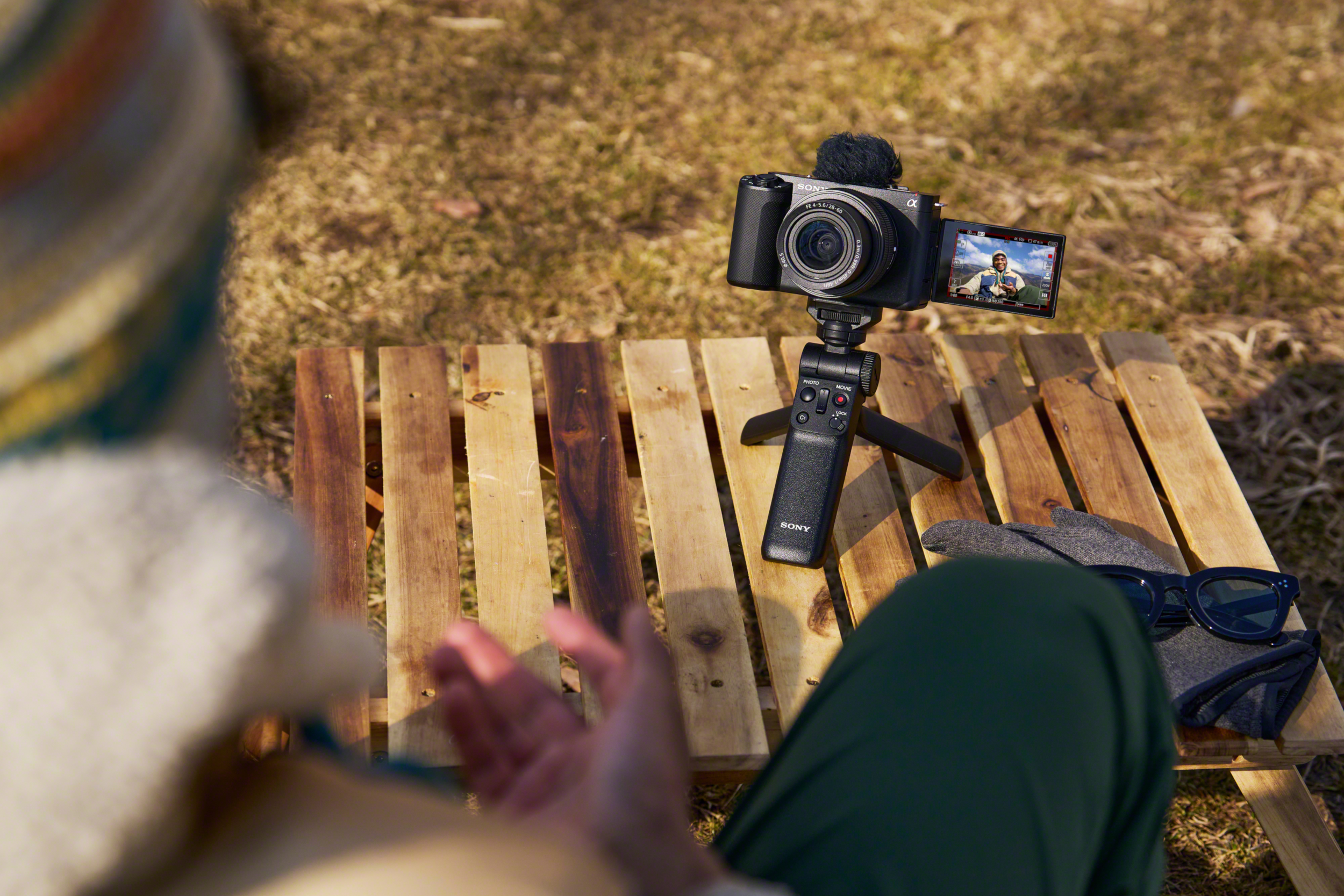 Person filmen mit Kamera auf Stativ, zeigt den Bildschirm, in einem Park.