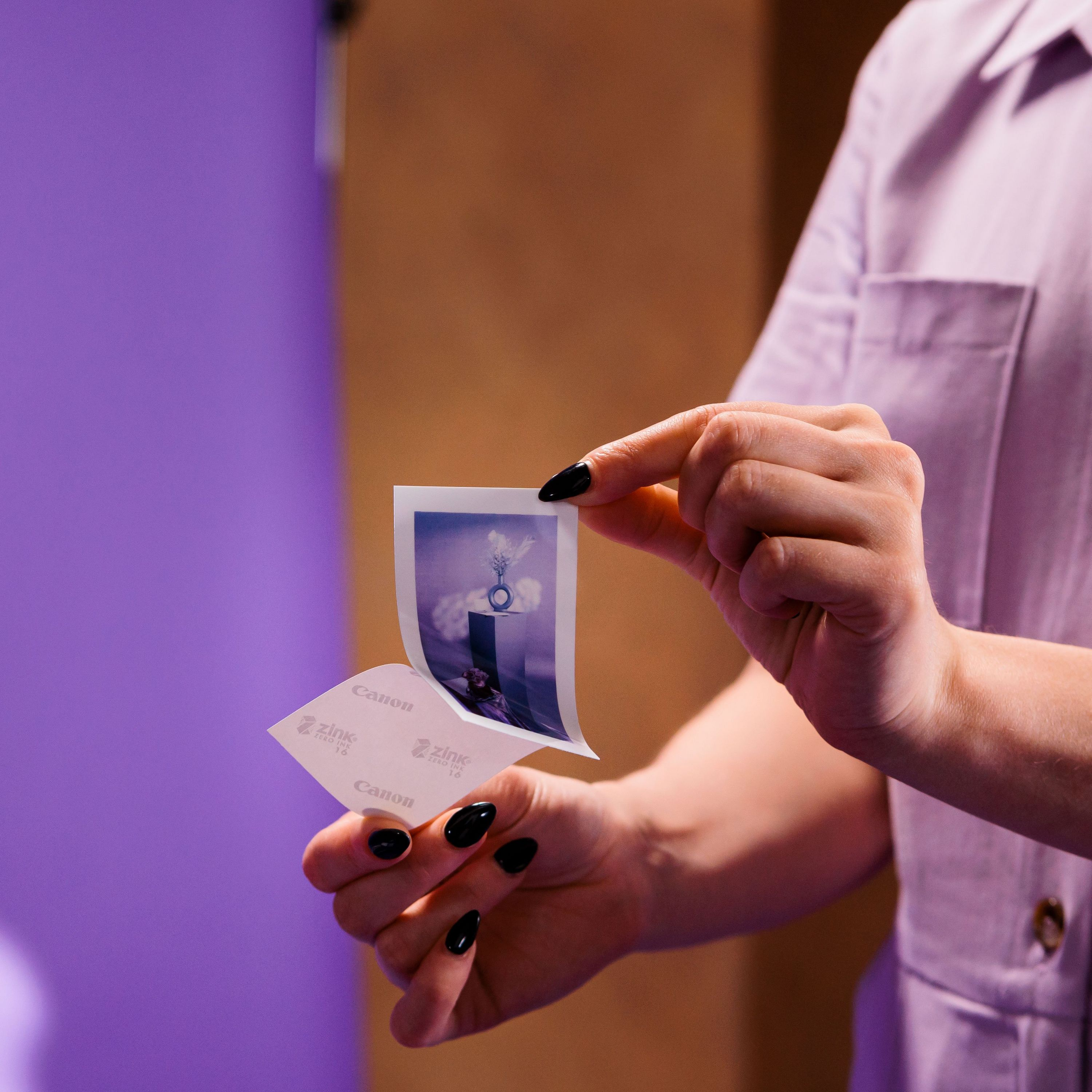 Donna che tiene in mano una foto stampata con sfondo viola e smalto nero.