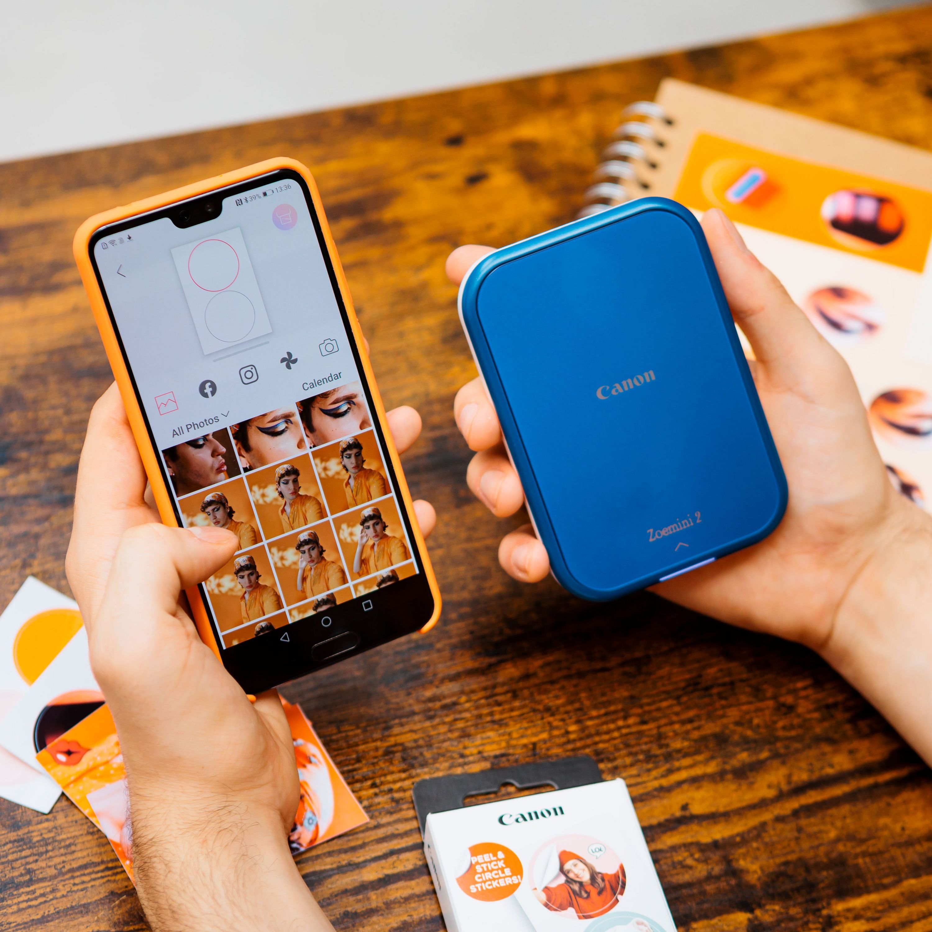 Mani che tengono uno smartphone e una stampante Canon Zoemini 2 blu con foto.