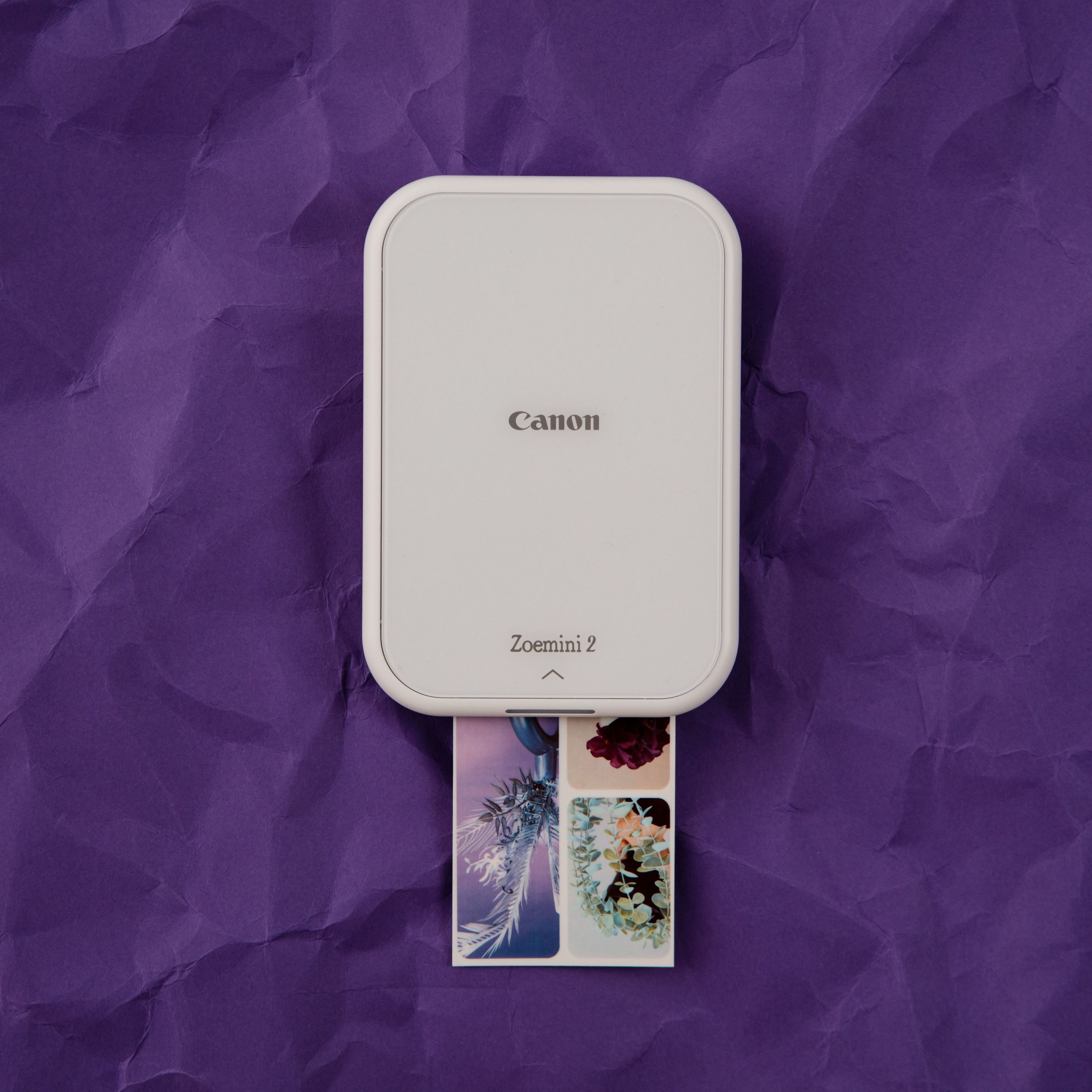 Una stampante Canon Zoemini 2 bianca con un'immagine stampata che emerge. Lo sfondo è viola.