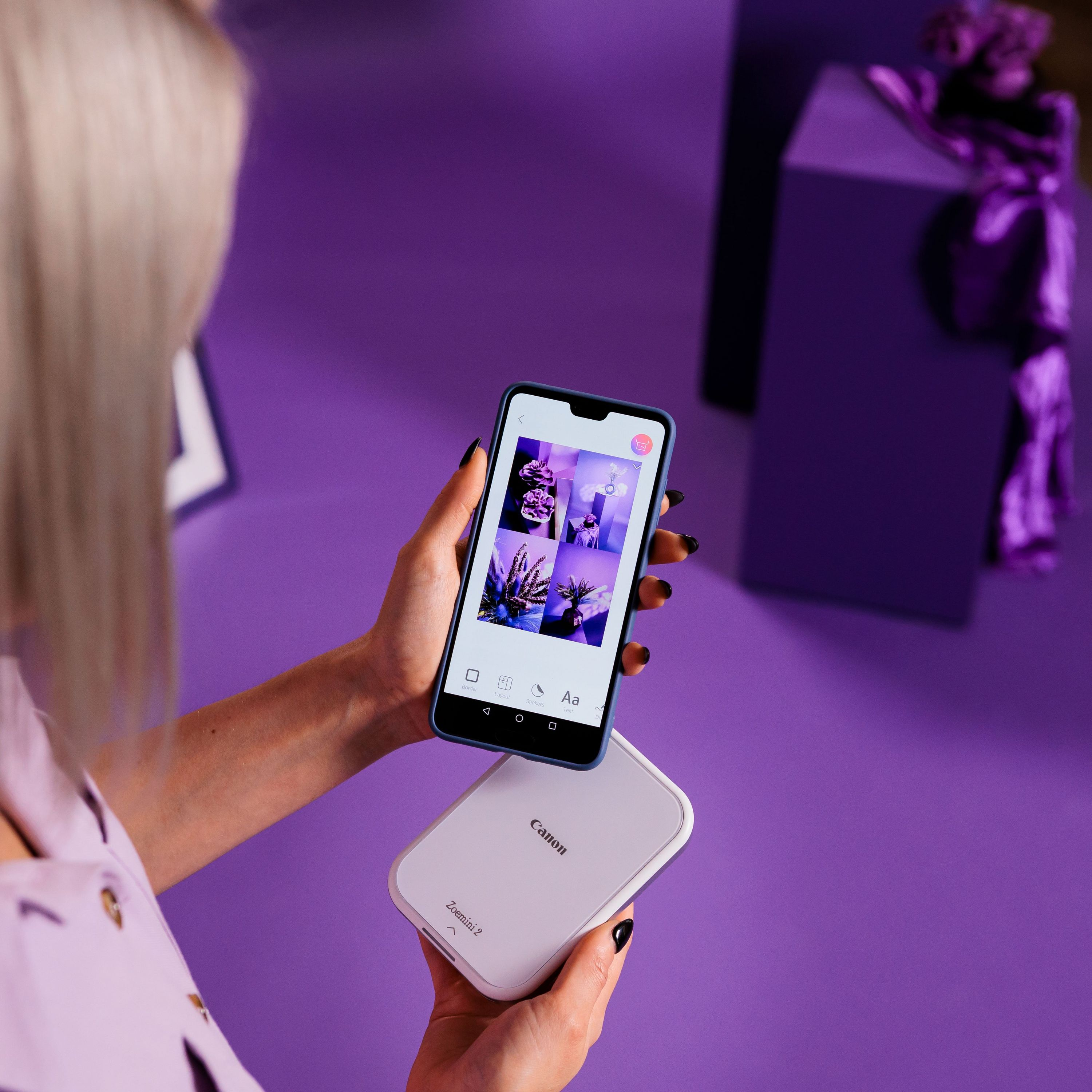 Una donna tiene in mano un telefono e una stampante bianca su una superficie viola, con forme viola sullo sfondo.