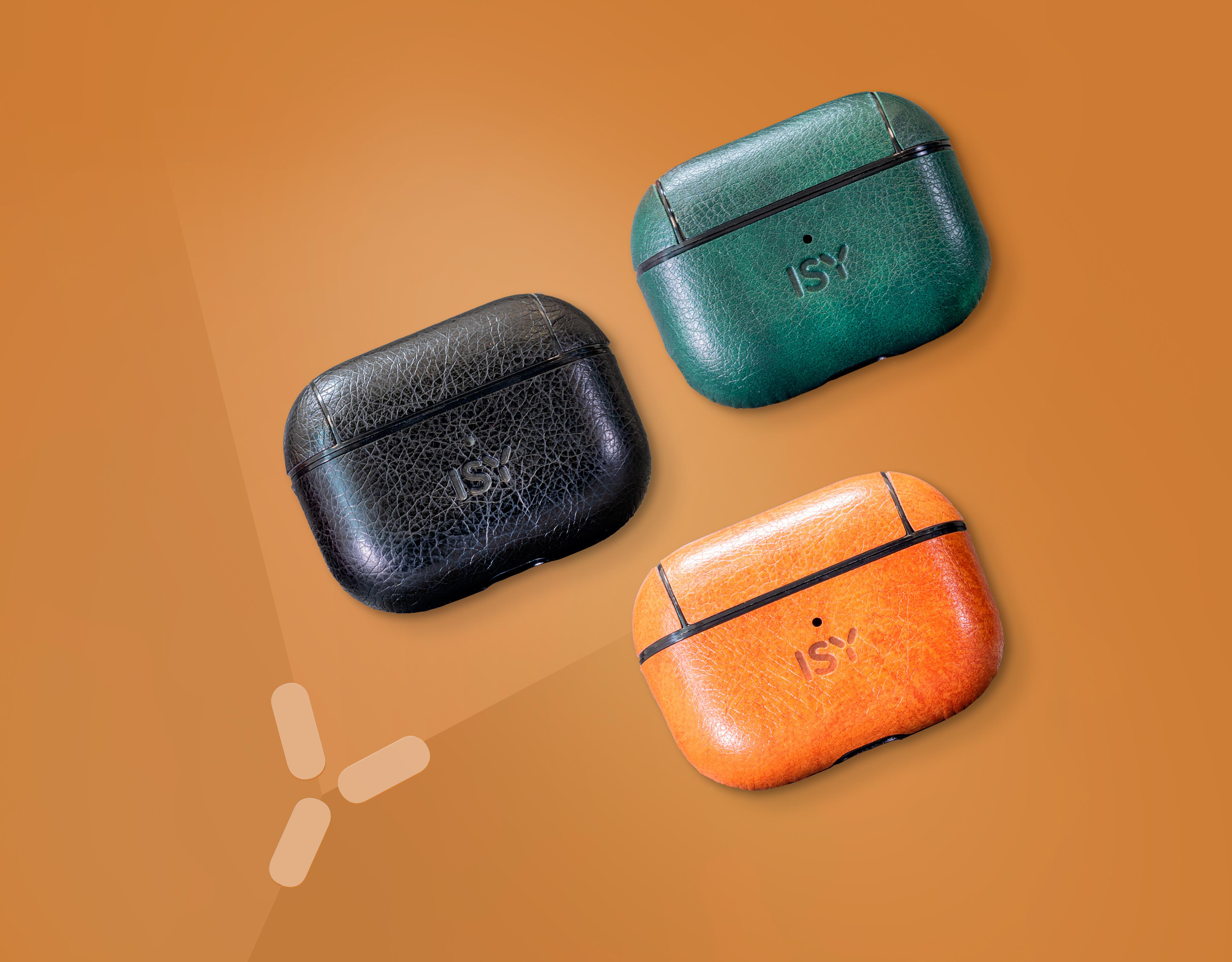 Drei Leder-AirPod-Hüllen in Schwarz, Grün und Orange auf brauner Oberfläche.