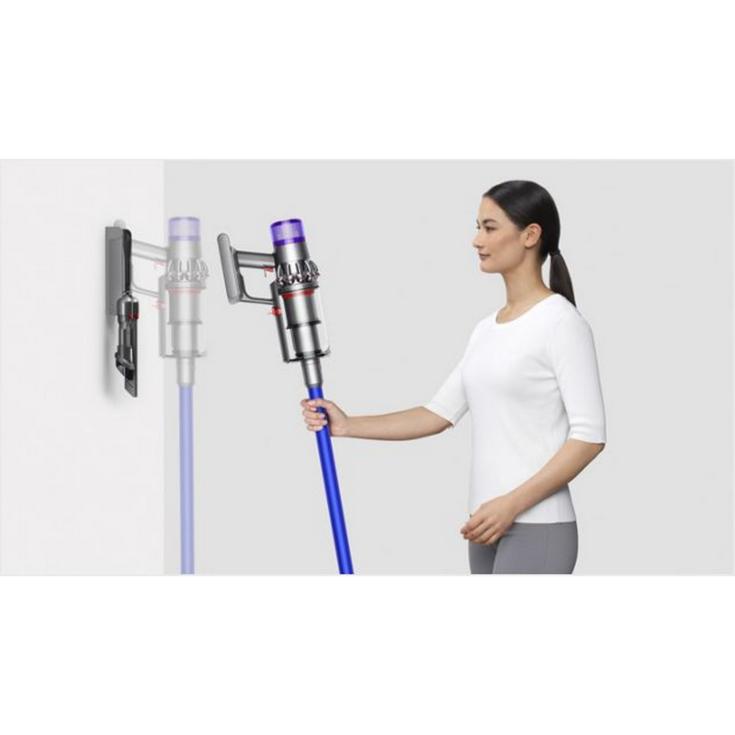 A woman holding a blue and silver vacuum cleaner, beside a wall mount.