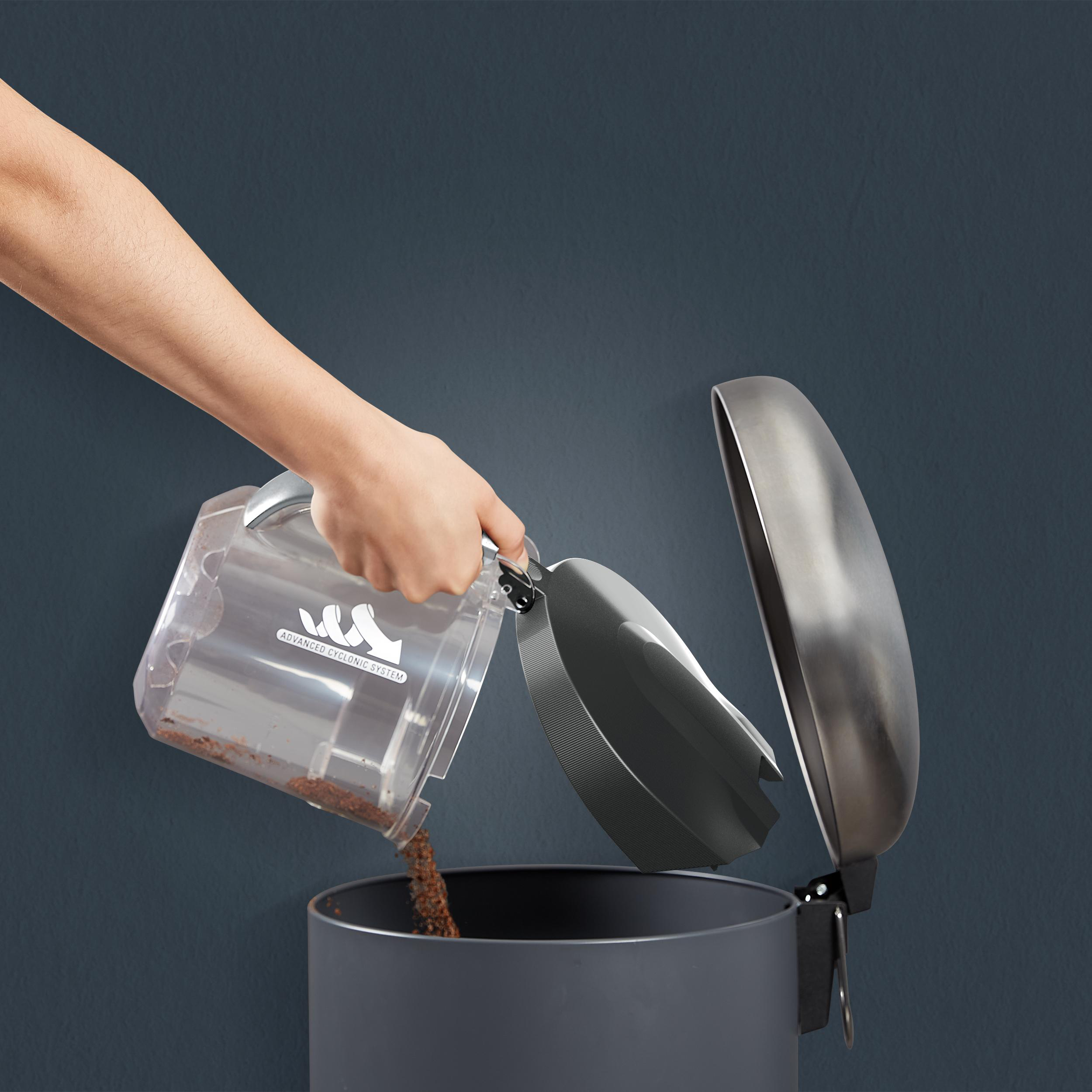 Eine Person entleert den Staubbehälter eines Staubsaugers in einen Mülleimer.