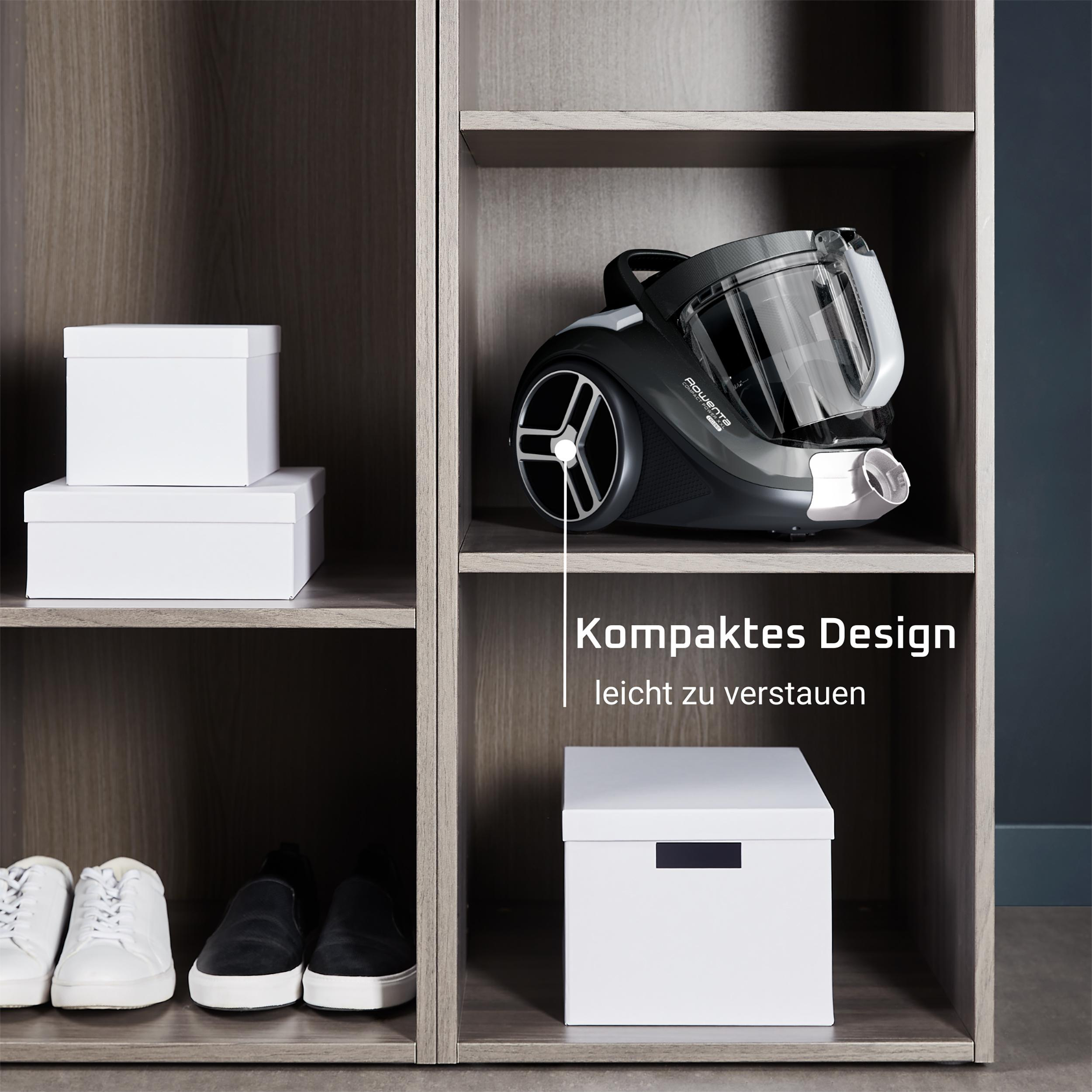 Ein Staubsauger und weiße Boxen auf Regalen in einem Holzschrank. Text: Kompaktes Design.