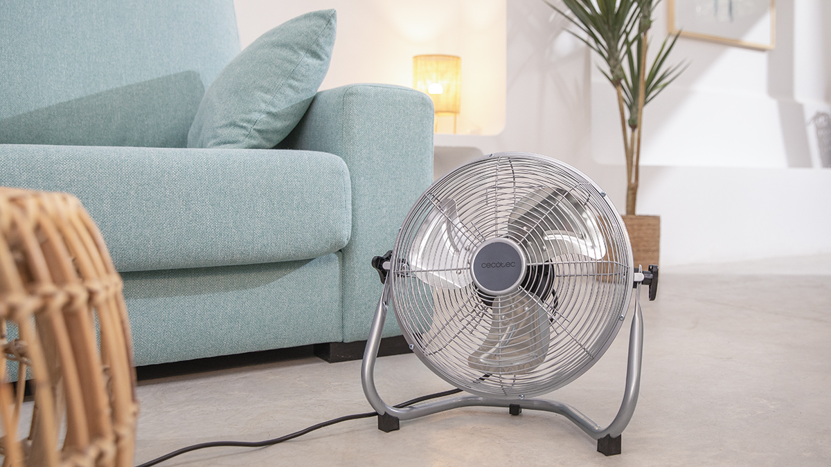 Un ventilador de metal plateado con una base negra está en una habitación. El ventilador está sobre un fondo blanco.