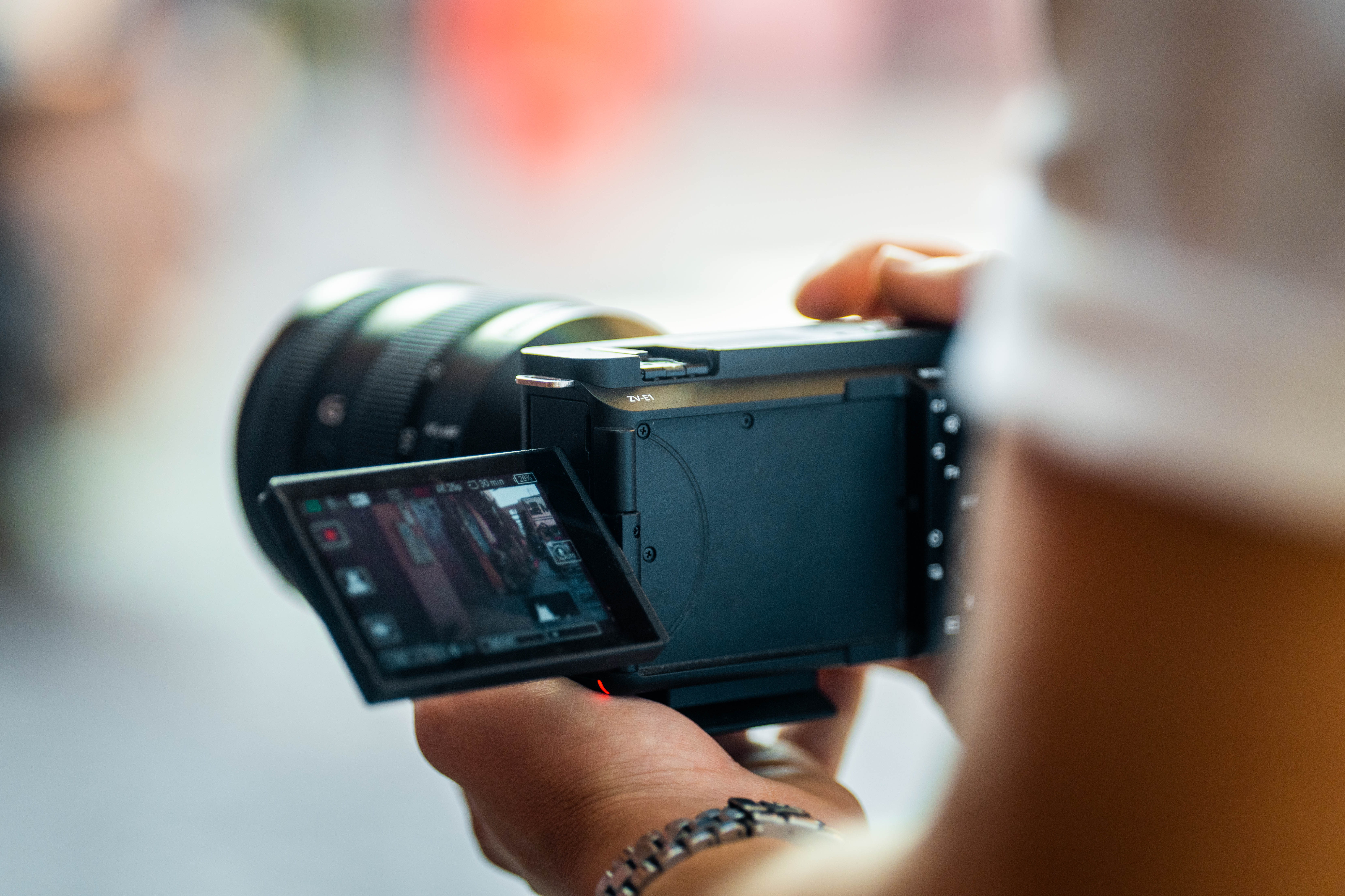 Una persona tiene in mano una fotocamera nera con uno schermo che mostra un'immagine. Lo sfondo è sfocato.