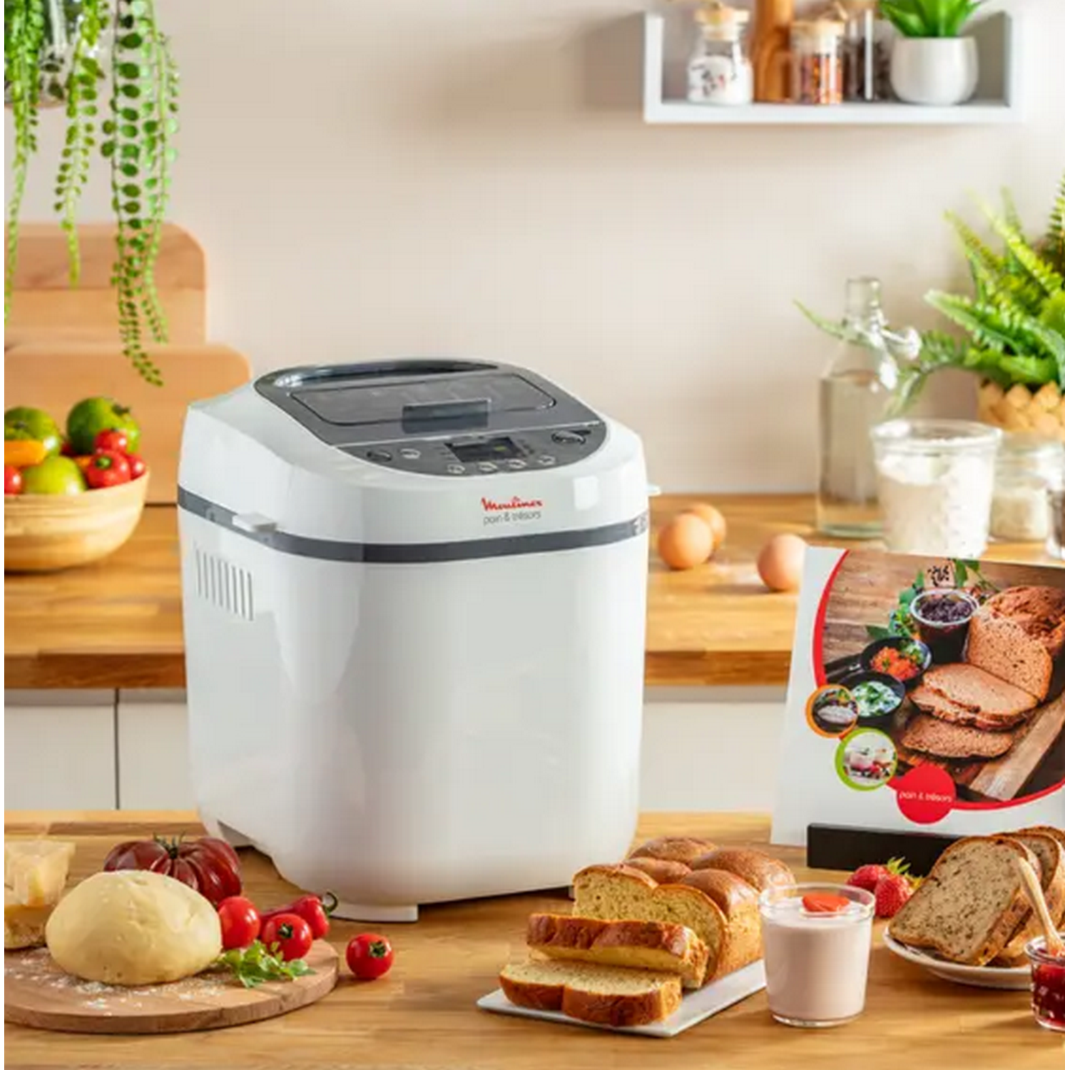 Een witte Moulinex broodbakmachine op een houten aanrecht met brood, ingrediënten en een kookboek.