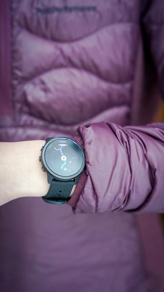Das Handgelenk einer Person mit einer schwarzen Uhr, Person trägt eine lila Jacke.
