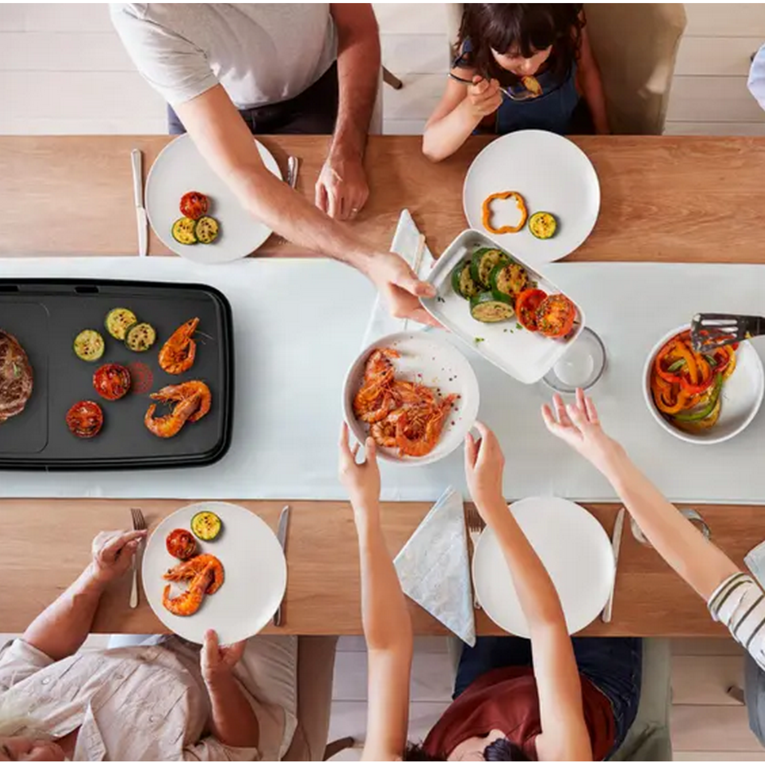 Des gens autour d'une table avec de la nourriture. Des crevettes et des légumes grillés sont visibles.