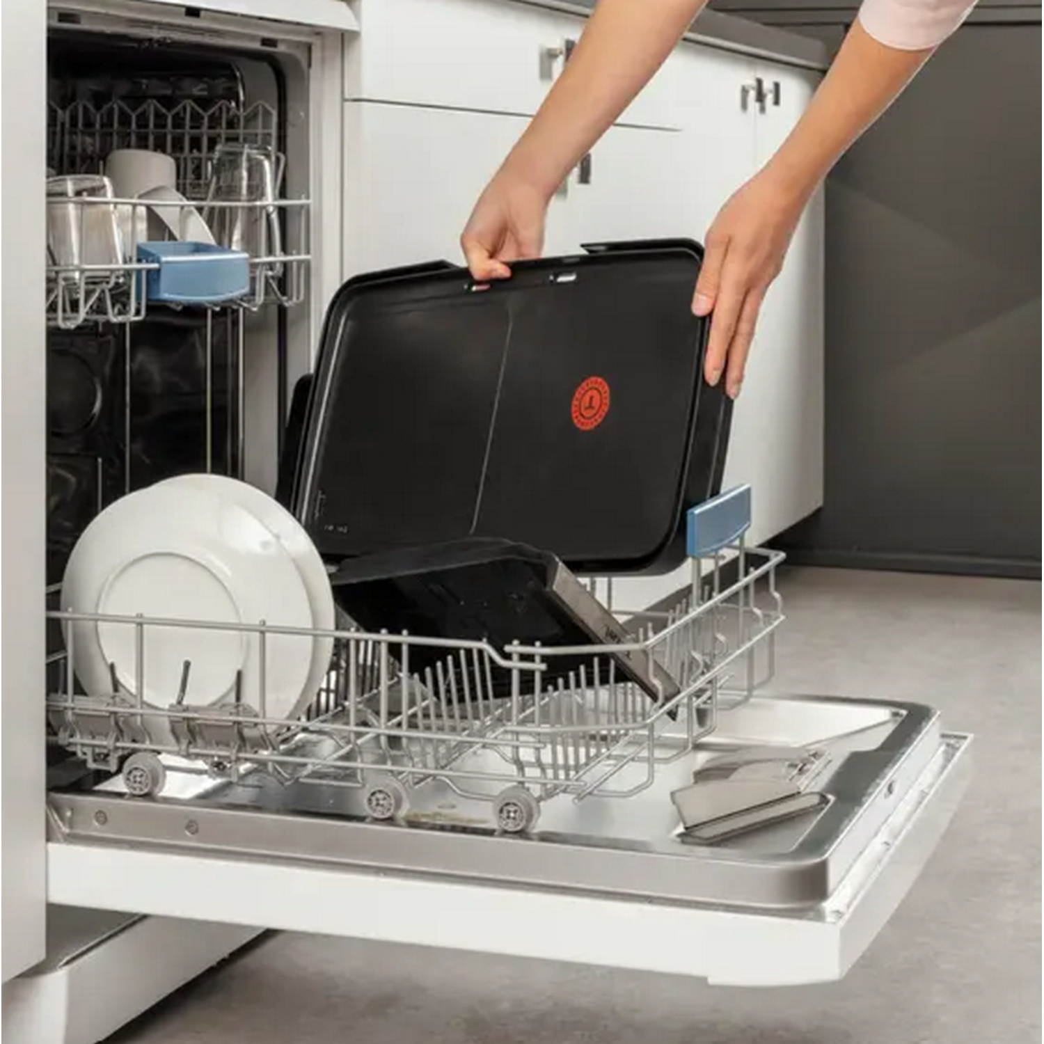 Une personne place un plateau noir dans un lave-vaisselle avec des plats et des verres à l'intérieur.