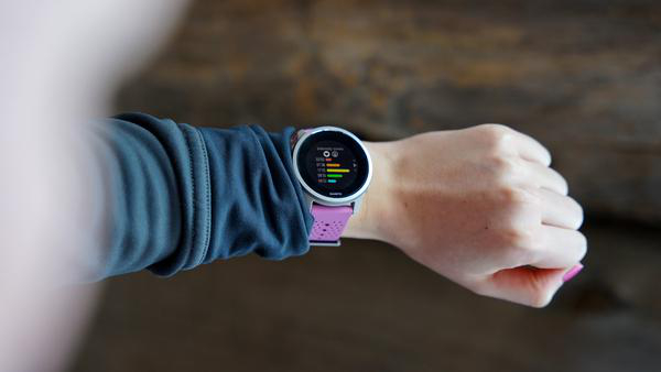 Handgelenk mit Smartwatch, die Daten anzeigt. Person trägt grauen Ärmel, pinkes Armband.