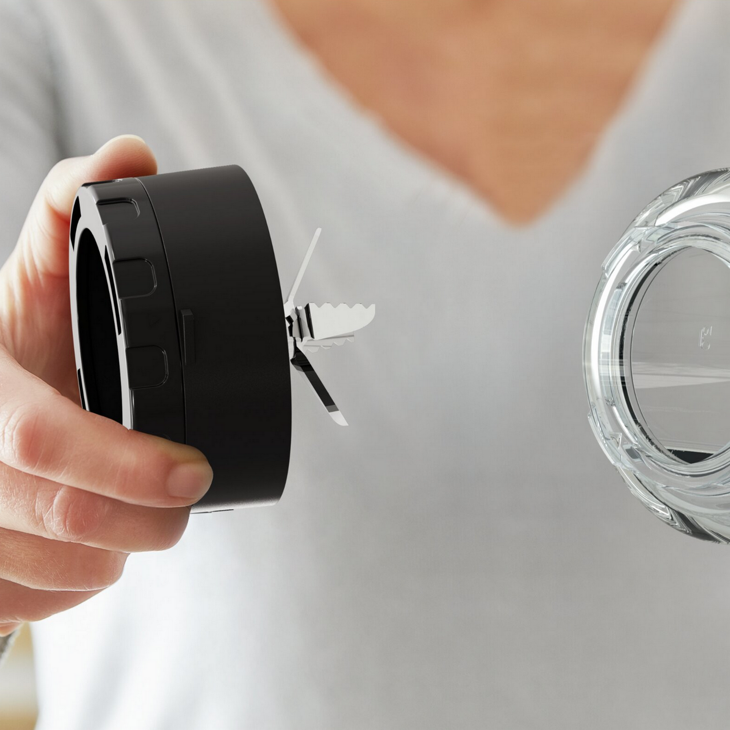 A person holding a black blender blade assembly next to a clear glass container.