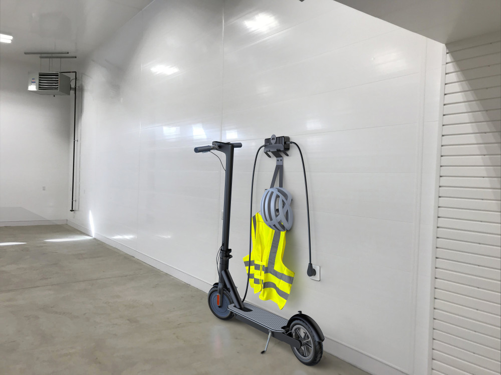 Egy elektromos robogó, sisak és mellény egy fehér falon lóg egy tiszta, üres szobában.