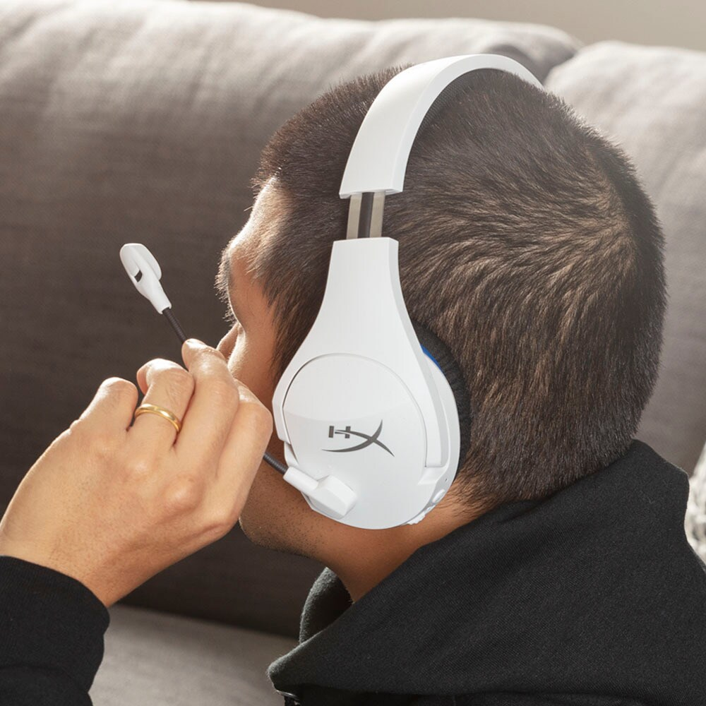Person mit weißem Gaming-Headset mit Mikrofon, sitzt auf einer Couch und schaut nach rechts.