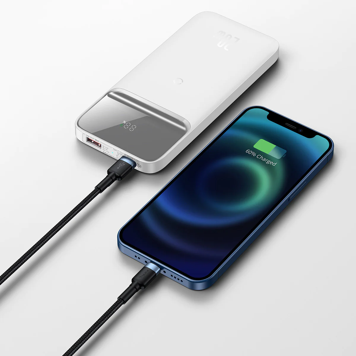 Beyaz bir powerbank, mavi bir iPhone'u şarj ediyor. Siyah kablo bağlı. Beyaz yüzey.