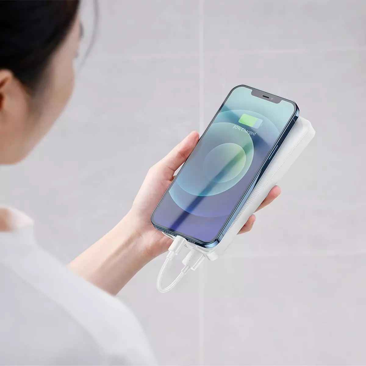 Beyaz bir güç bankasıyla şarj olan bir telefonu tutan bir kişi.