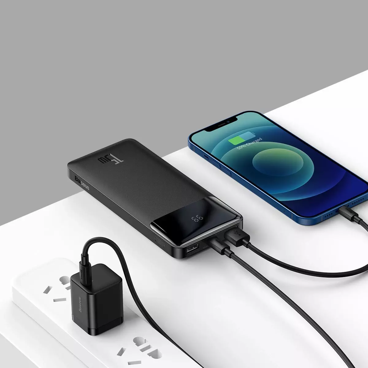 Siyah bir güç bankası bir telefonu şarj ediyor ve bir duvar prizine takılı küçük bir siyah şarj cihazı.