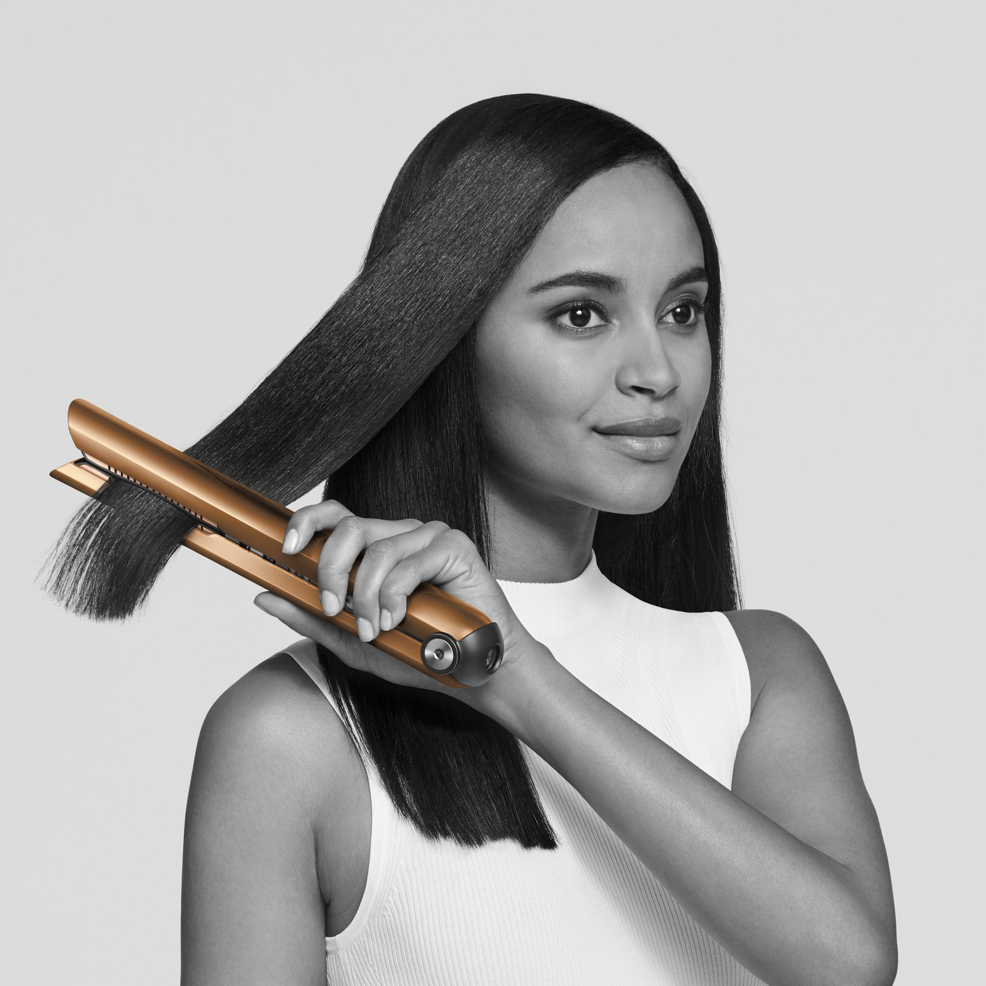 Frau benutzt einen goldenen Haarglätter auf ihrem schwarzen Haar.
