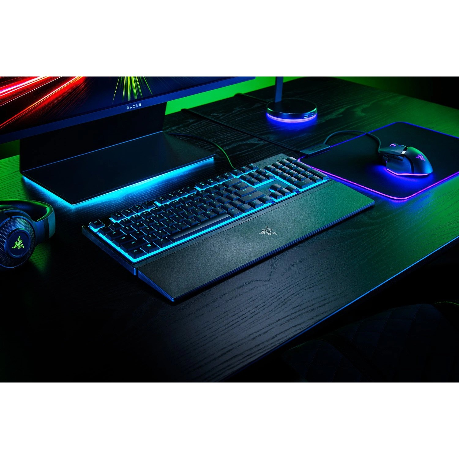 Black gaming keyboard with blue lighting on a dark desk. A mouse and monitor are also present.