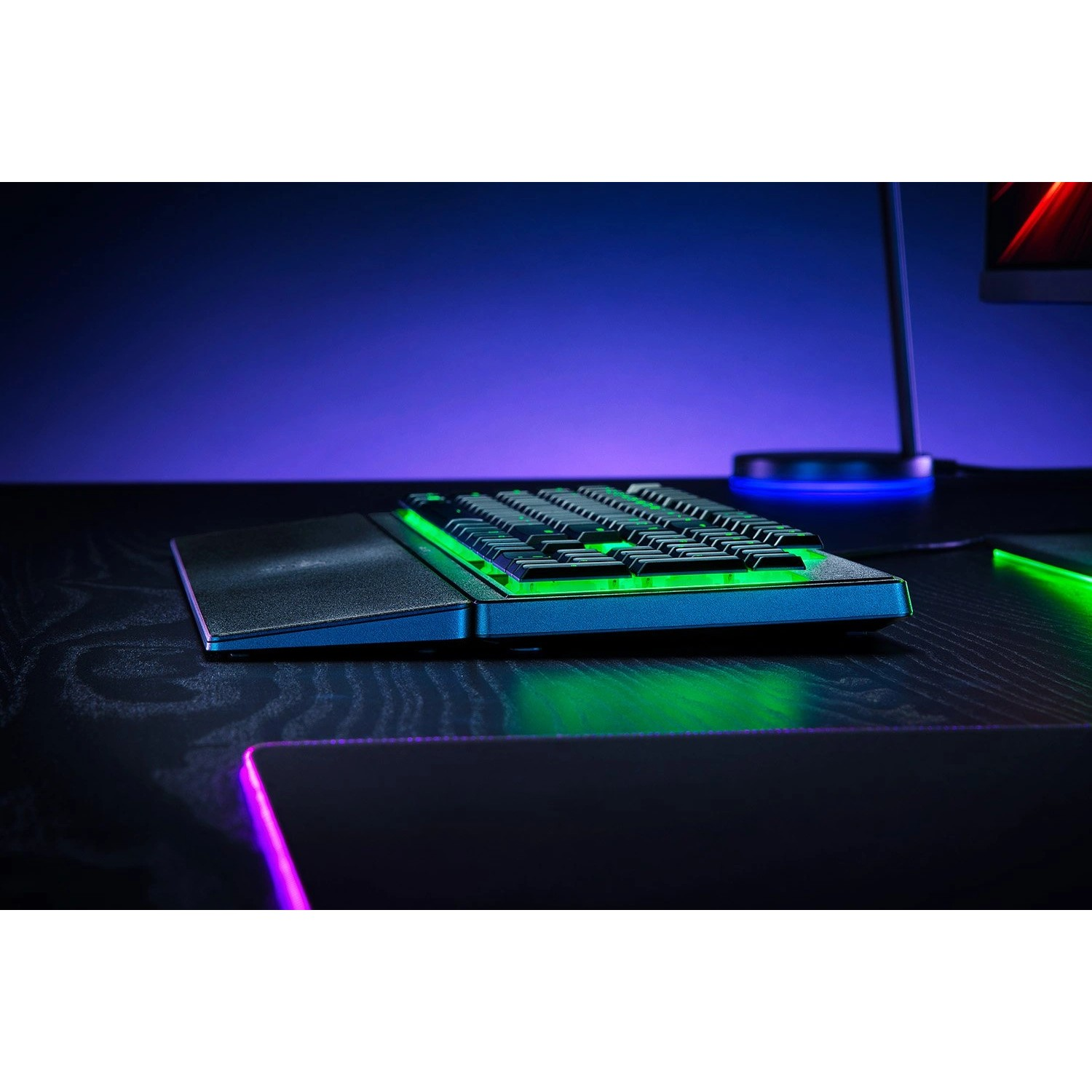Gaming keyboard with green lights on desk with other objects.